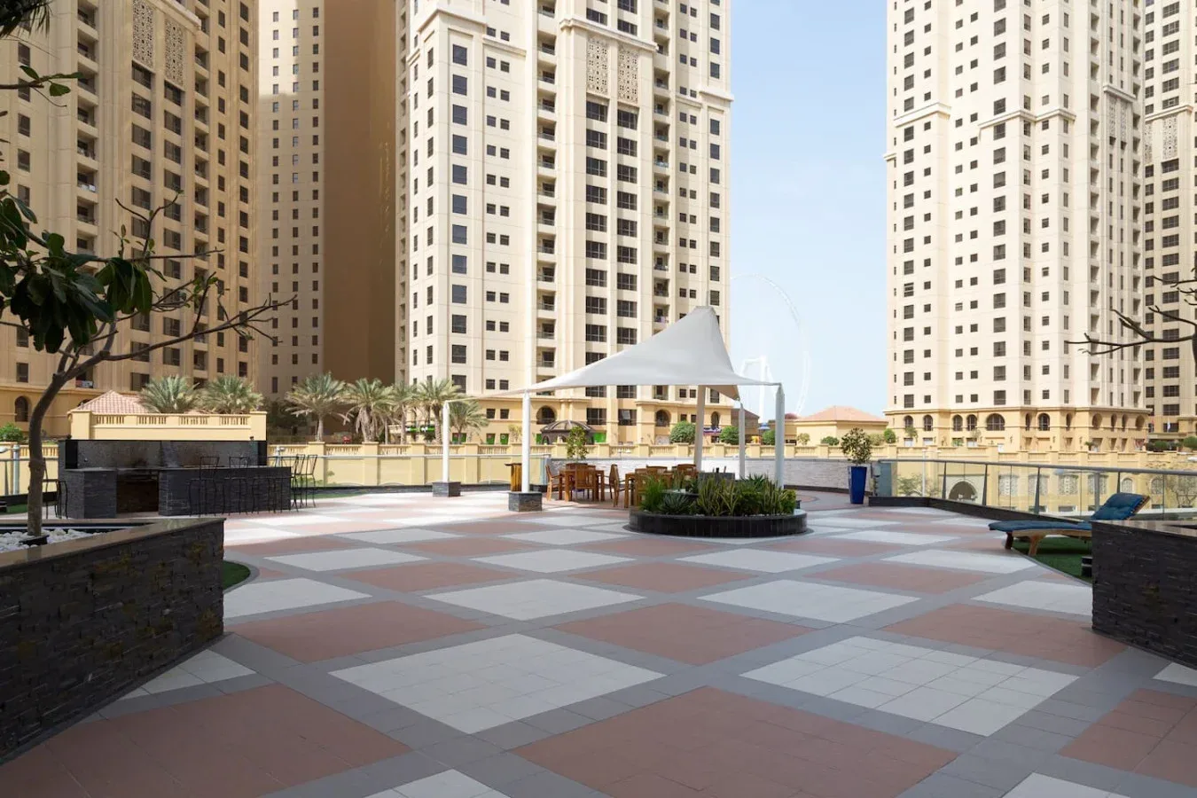 Una terraza al aire libre con pavimento estampado, asientos y edificios altos al fondo.