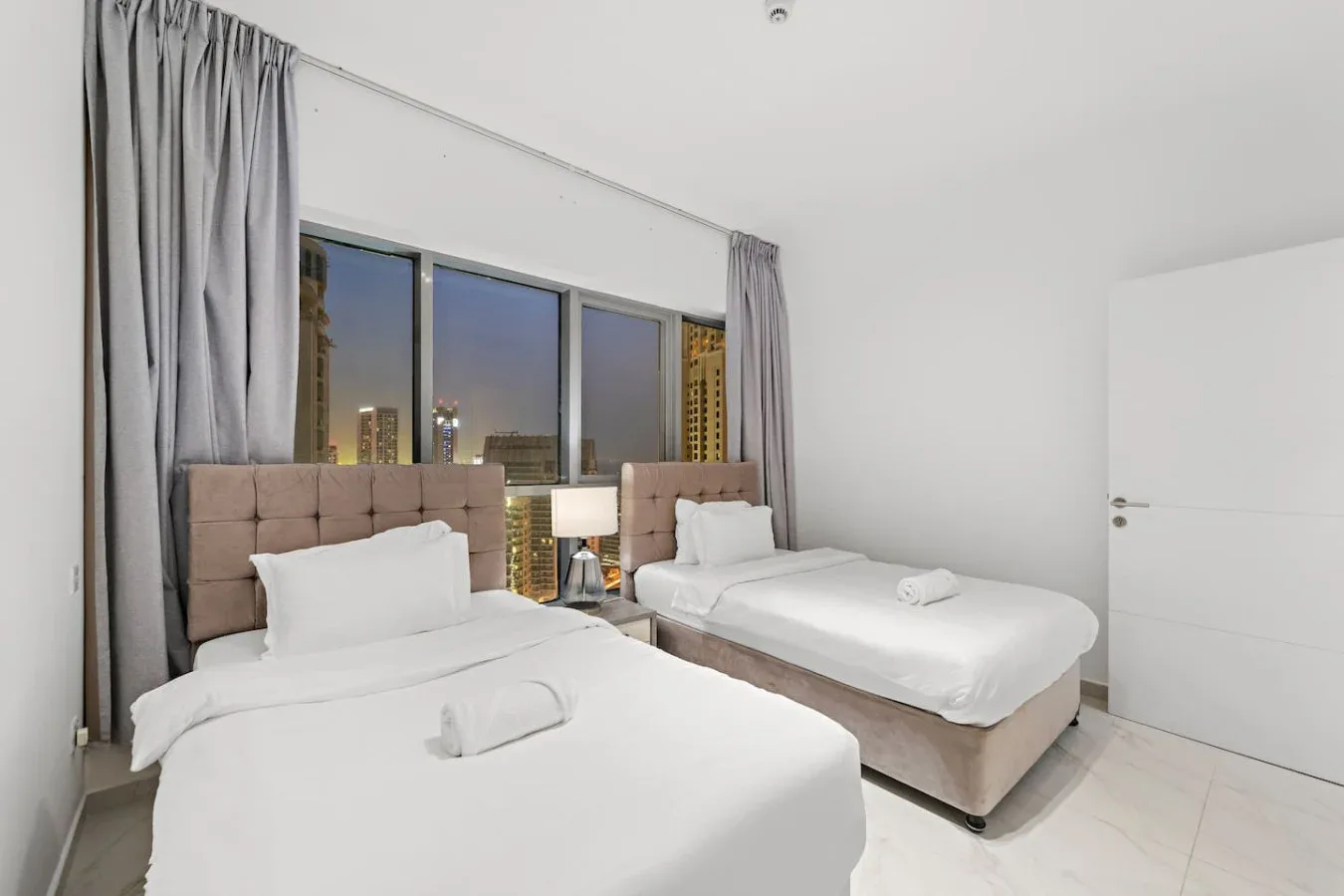 Un dormitorio con dos camas, ropa de cama blanca y una ventana grande.