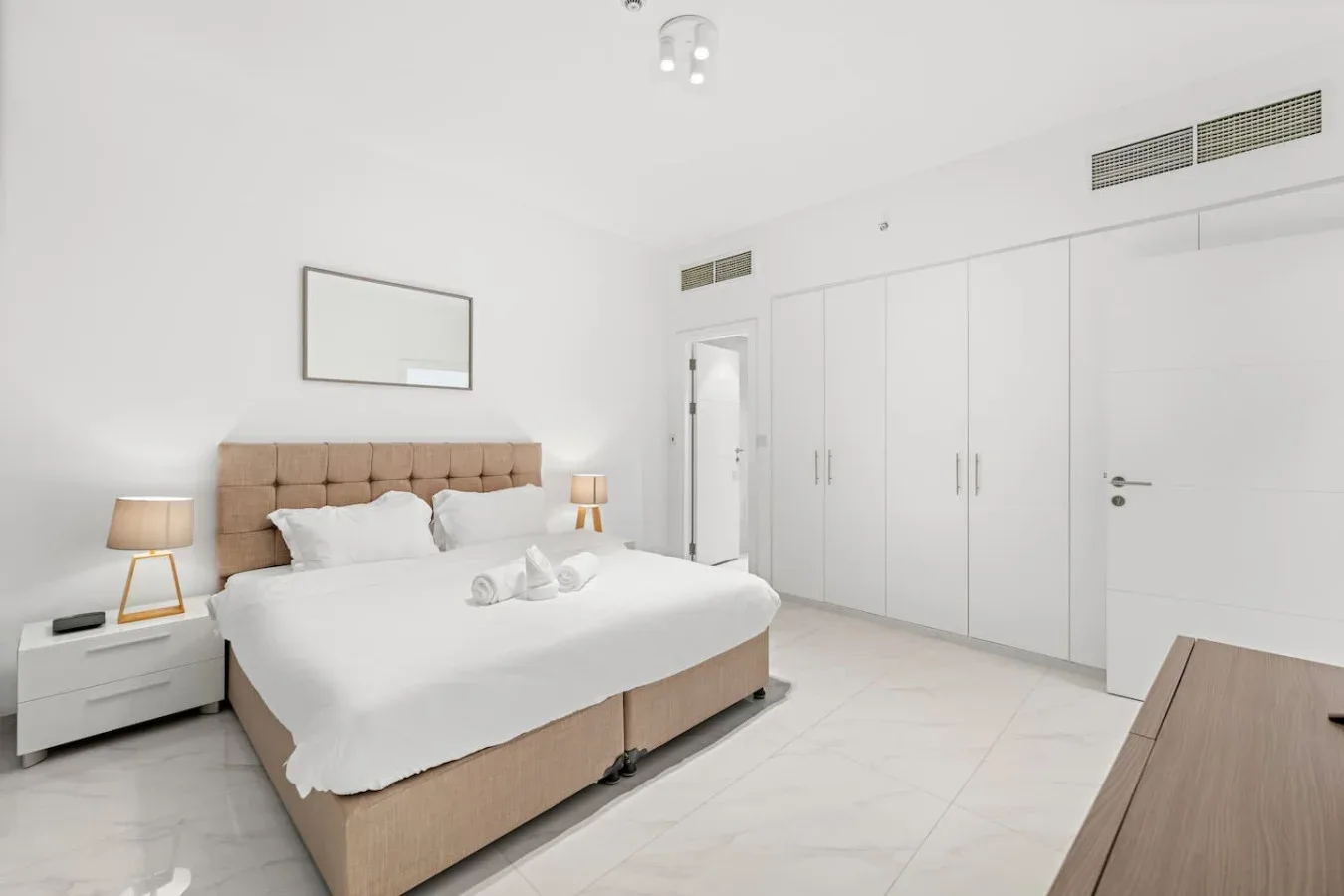 Un dormitorio luminoso con una cama, mesitas de noche y armarios empotrados blancos.