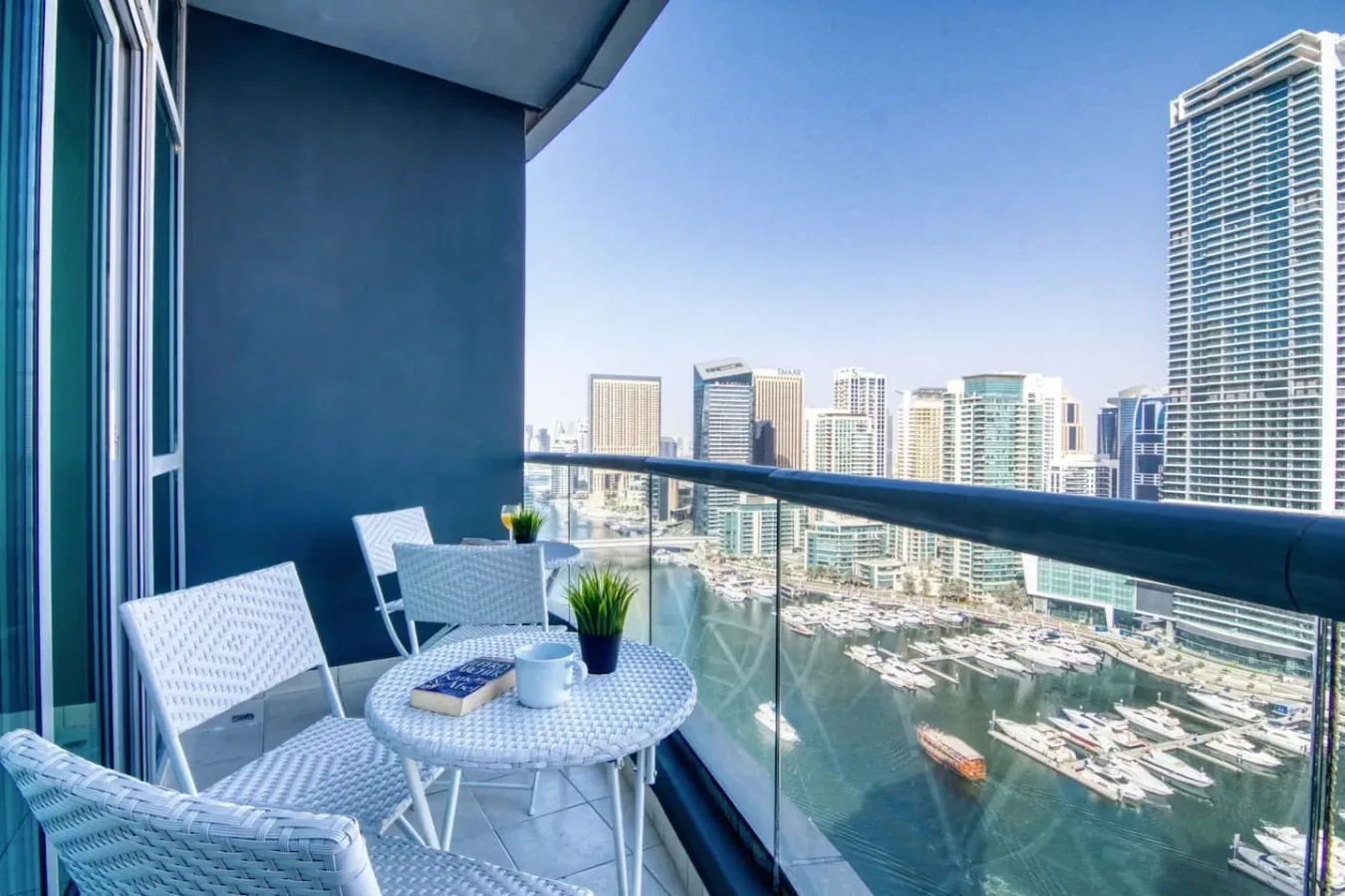 Una zona de estar en un balcón da a una marina y al horizonte urbano.