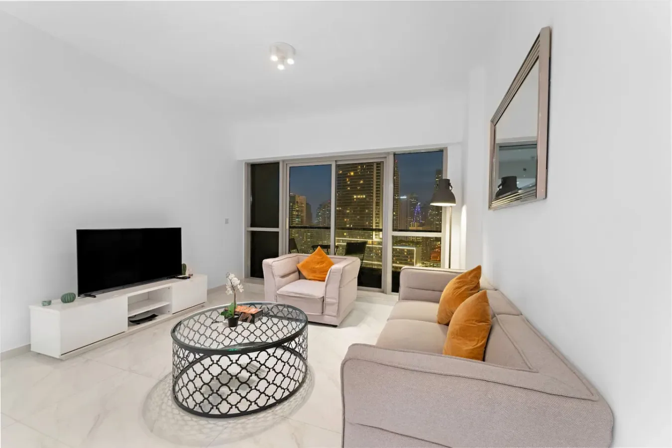 Una sala luminosa con asientos, un televisor y grandes ventanas con vistas a las luces de la ciudad.