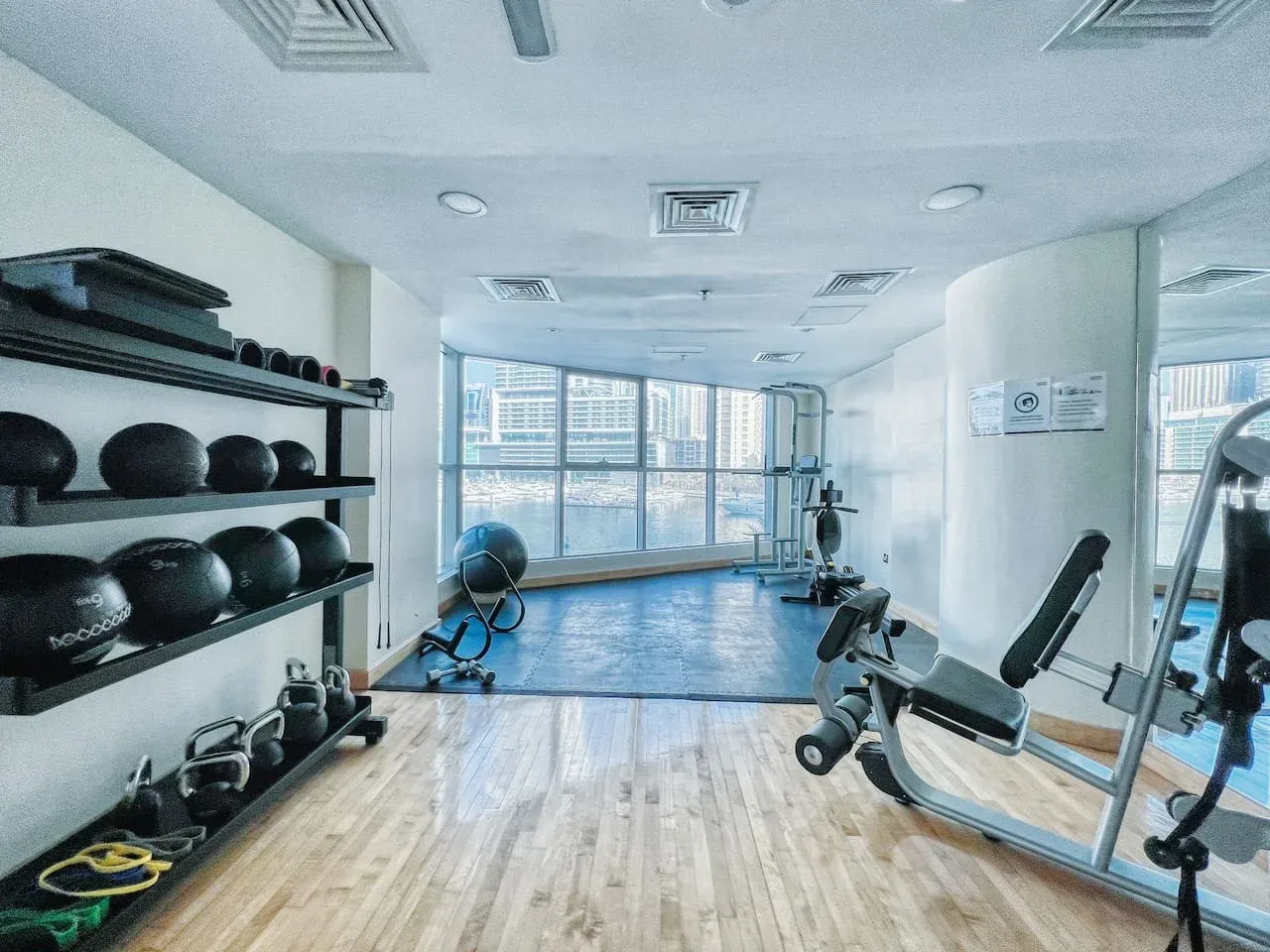 Un gimnasio con máquinas de ejercicio, pesas y grandes ventanales.