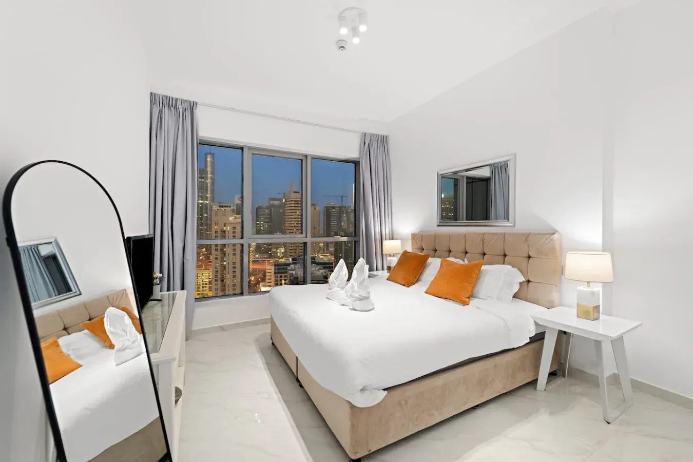 Un dormitorio luminoso con una cama grande junto a una ventana con vistas a edificios.