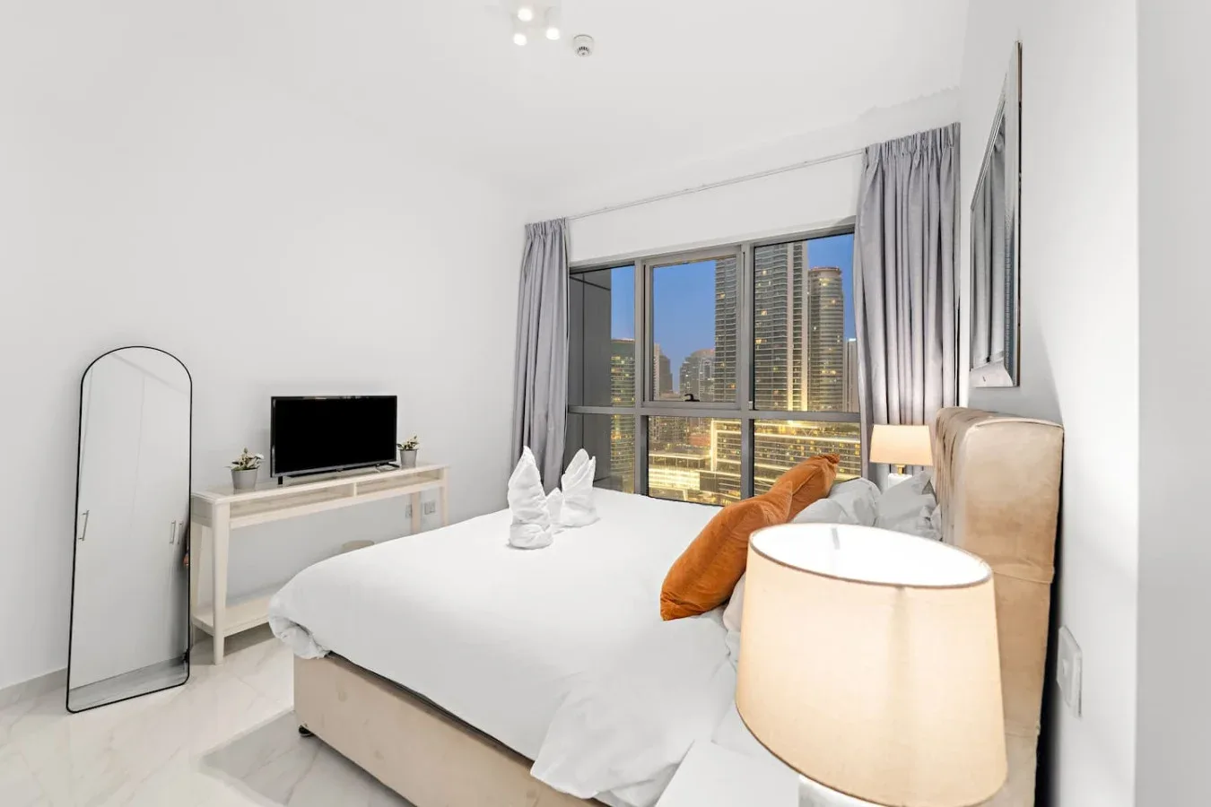Un dormitorio luminoso con una cama grande y una ventana con vistas a edificios de la ciudad.