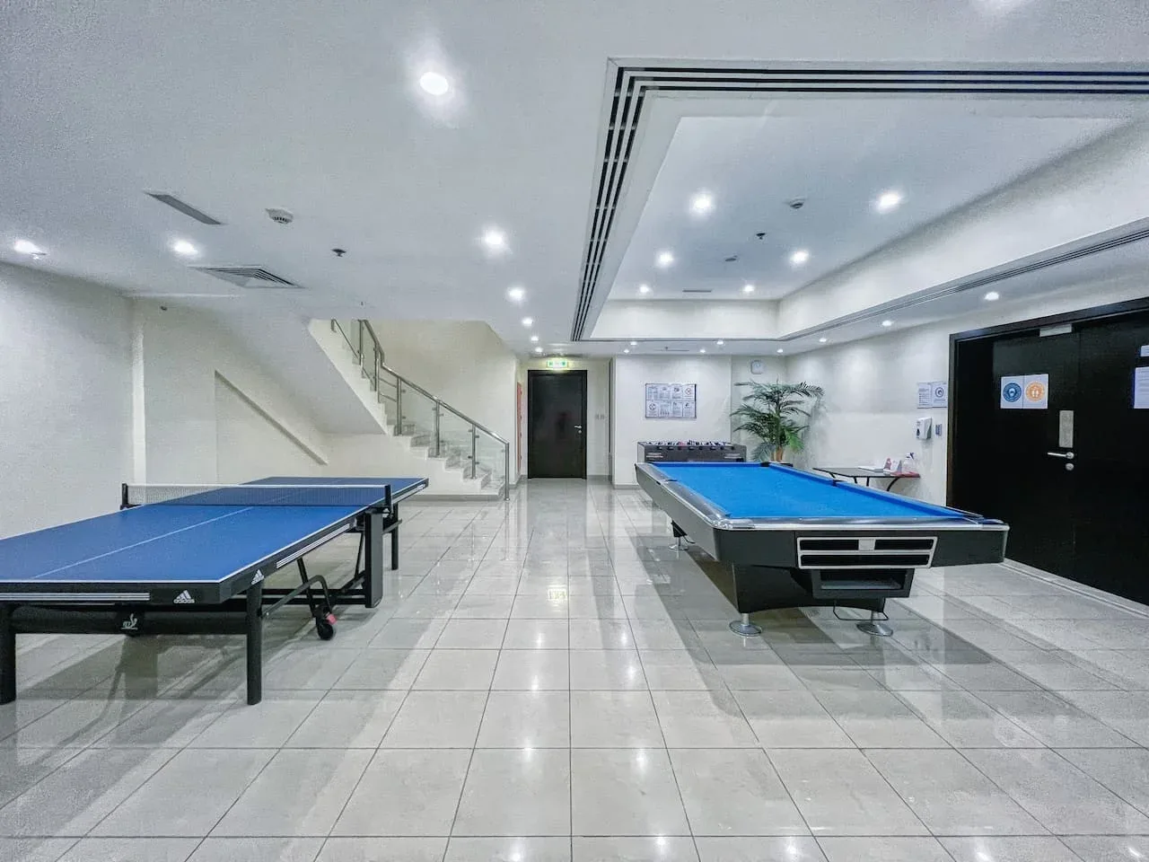Una sala recreativa interior con mesas de ping-pong azules sobre un suelo de baldosas.