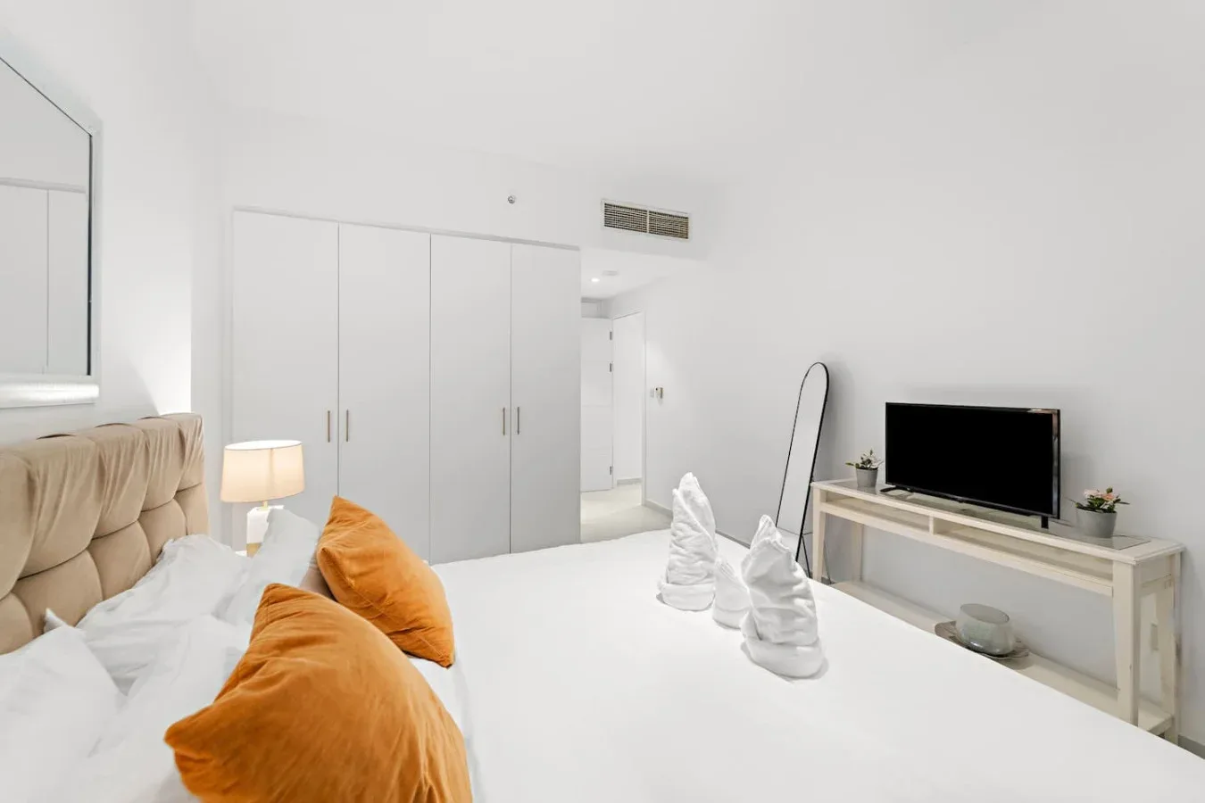 Un dormitorio luminoso con una cama, armarios blancos y un televisor sobre una consola.