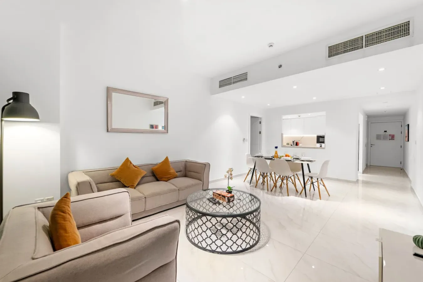 Una luminosa sala de estar y comedor diáfanos con asientos beige alrededor de una mesa de centro de vidrio.