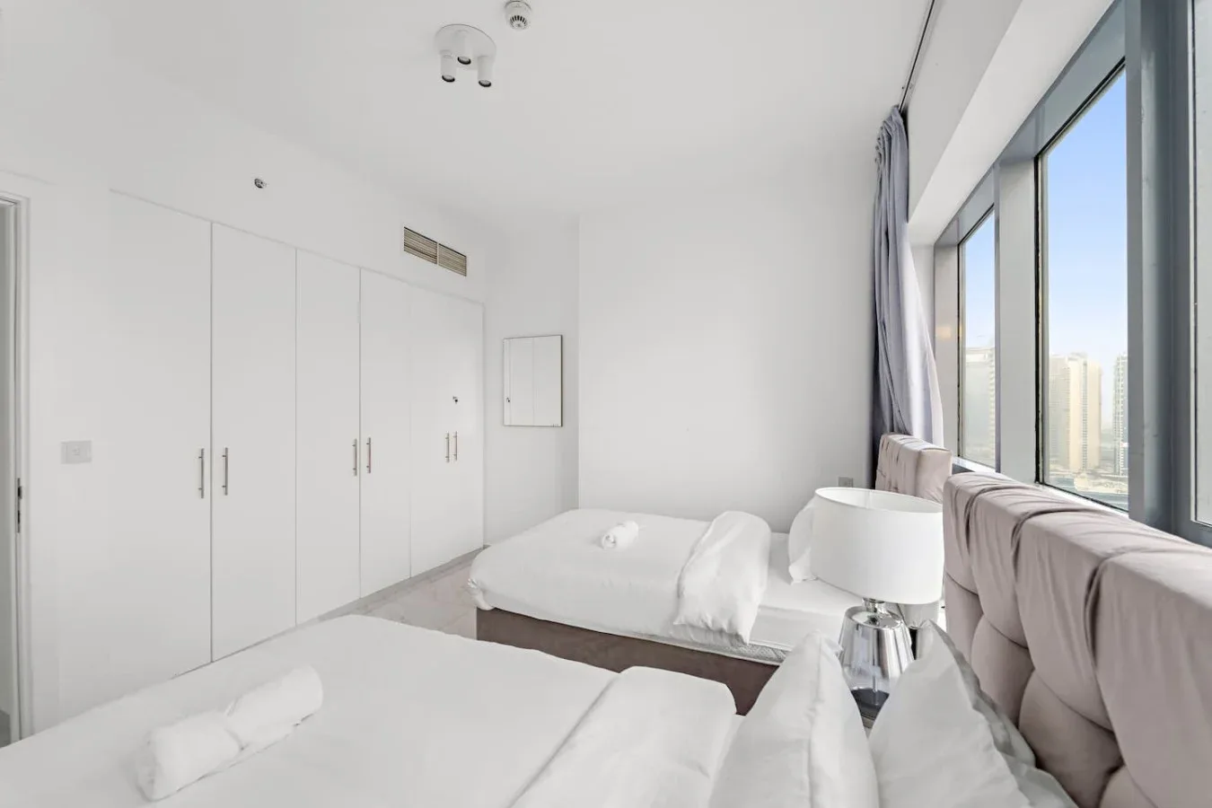 Un dormitorio luminoso con camas junto a grandes ventanas.