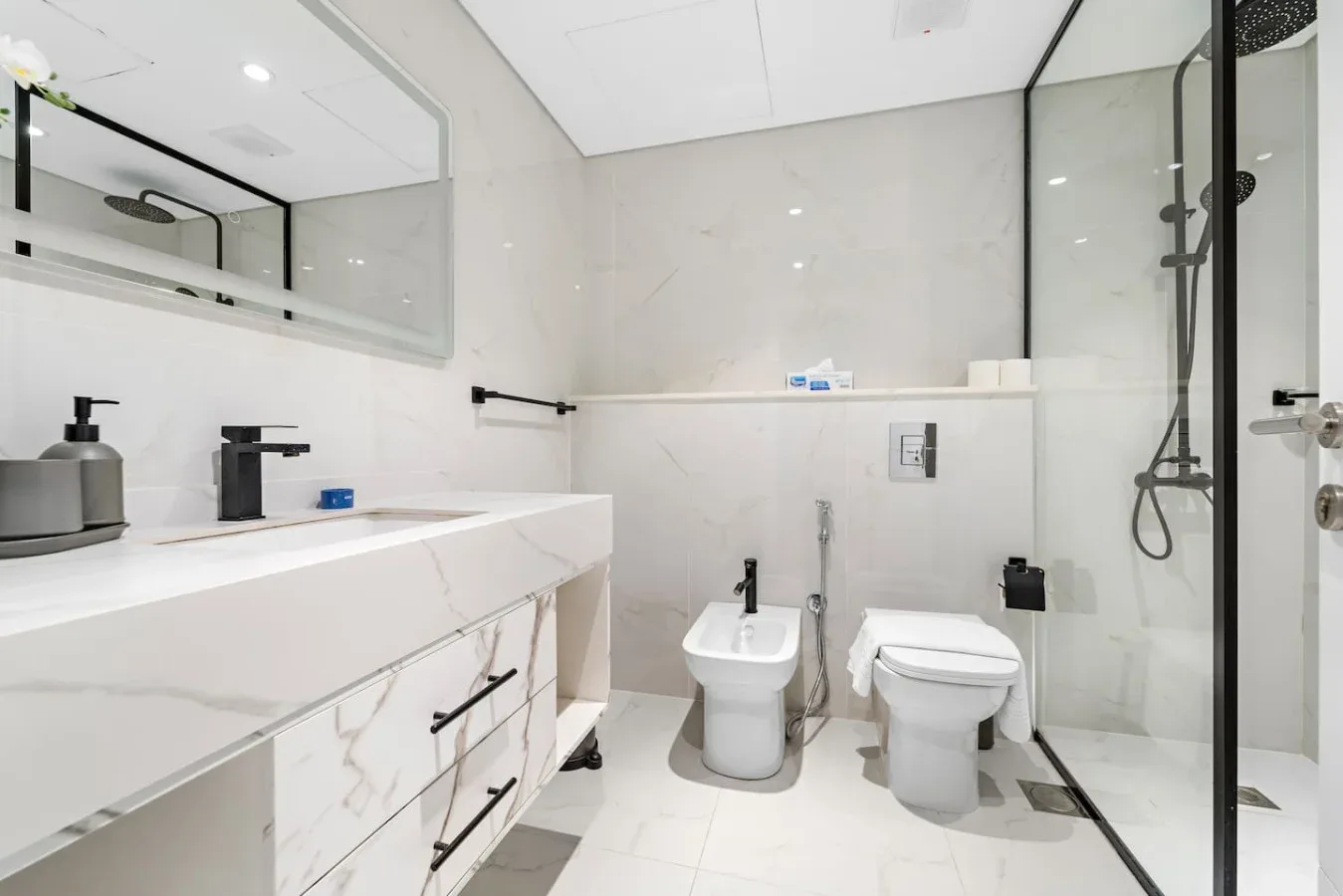 Un baño luminoso con un tocador largo y una ducha con mampara de vidrio.