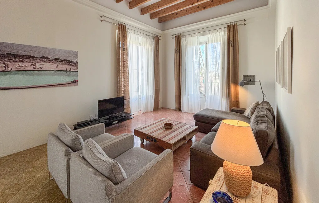 Una sala de estar con asientos alrededor de una mesa de centro de madera y ventanas altas.