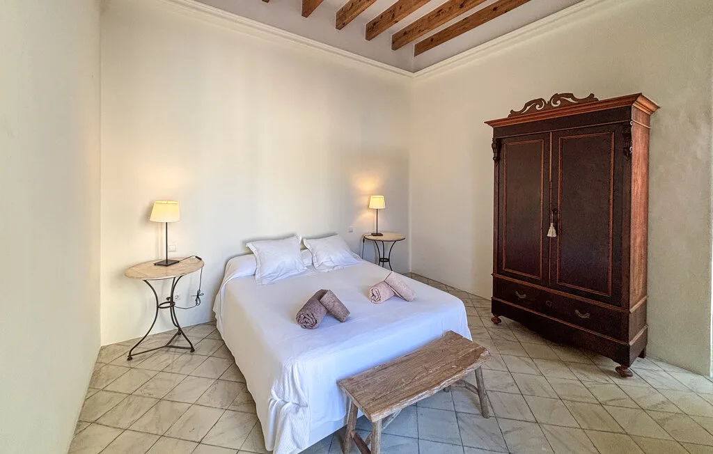 Un dormitorio con una cama blanca, mesitas de noche y un armario de madera oscura.