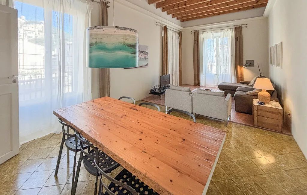 Una luminosa sala de estar y comedor tiene una mesa de madera y asientos junto a grandes ventanas.