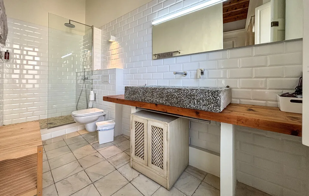 Un baño revestido de azulejos con ducha de vidrio, inodoro y tocador largo.