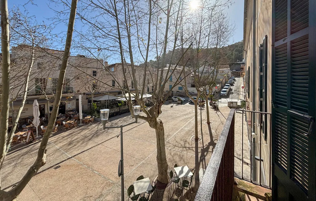 Vista soleada de un patio pavimentado con árboles sin hojas y edificios cercanos.