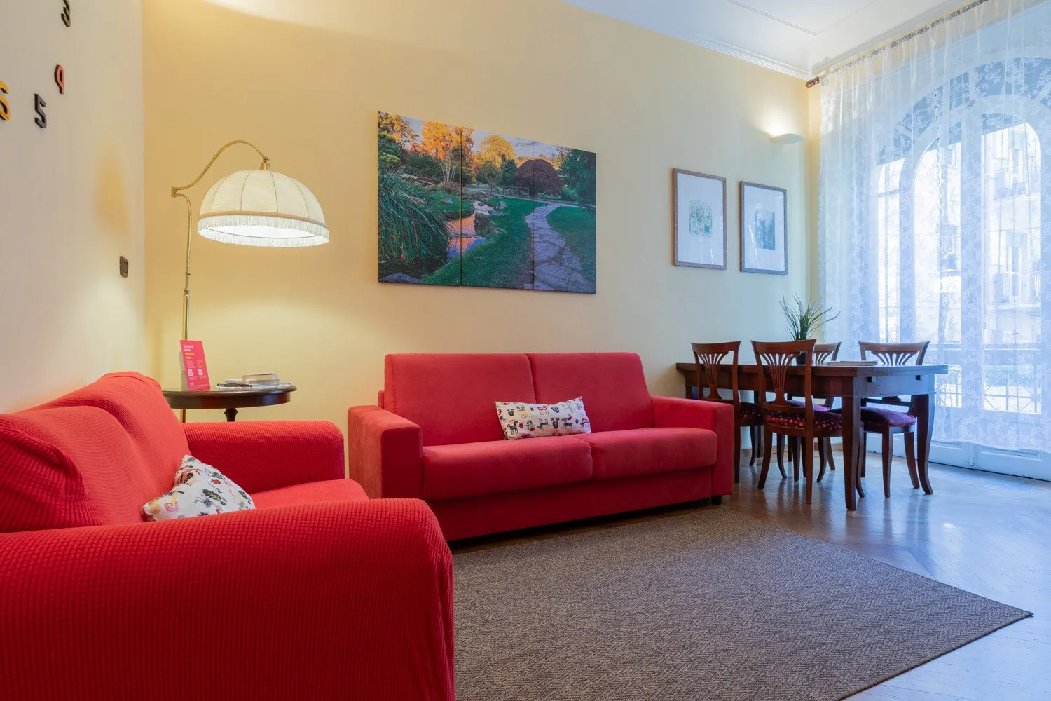 Una sala de estar con asientos rojos, una mesa de comedor y grandes ventanas con cortinas.