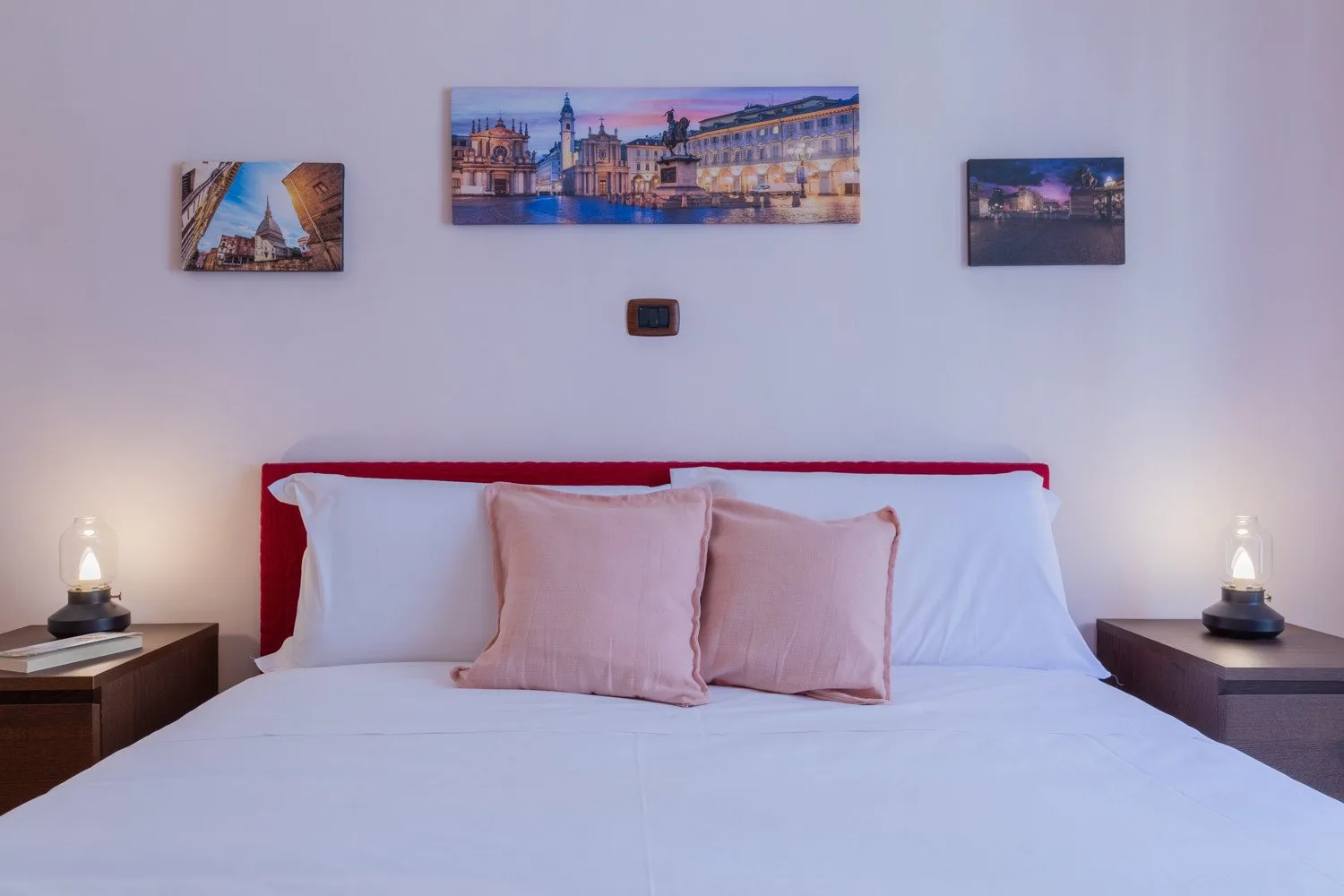 Un dormitorio con una cama tendida, almohadas claras y cuadros enmarcados sobre el cabecero.