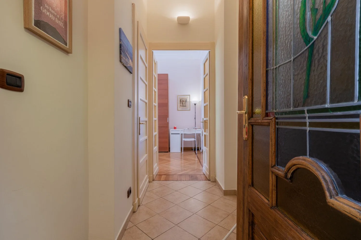 Un pasillo con suelo de baldosas conduce a una habitación luminosa con una mesa pequeña y sillas.
