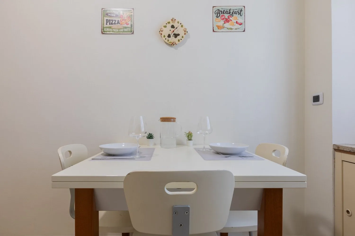Un comedor con una mesa blanca y sillas bajo pequeños adornos de pared.