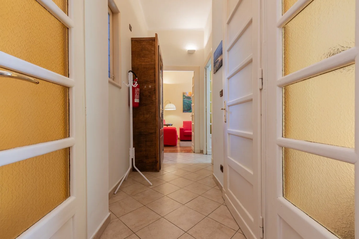 Un pasillo con suelo de baldosas conduce, por puertas abiertas, a una sala con asientos rojos.