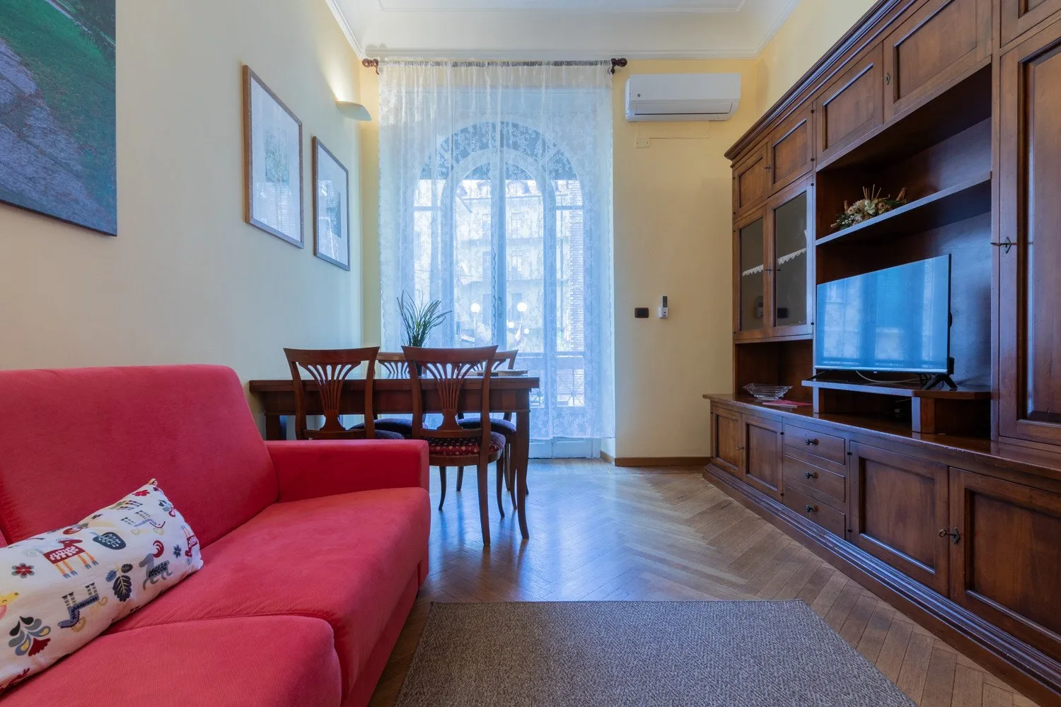 Una sala de estar con un sofá rojo, una mesa de comedor y un mueble para televisión.