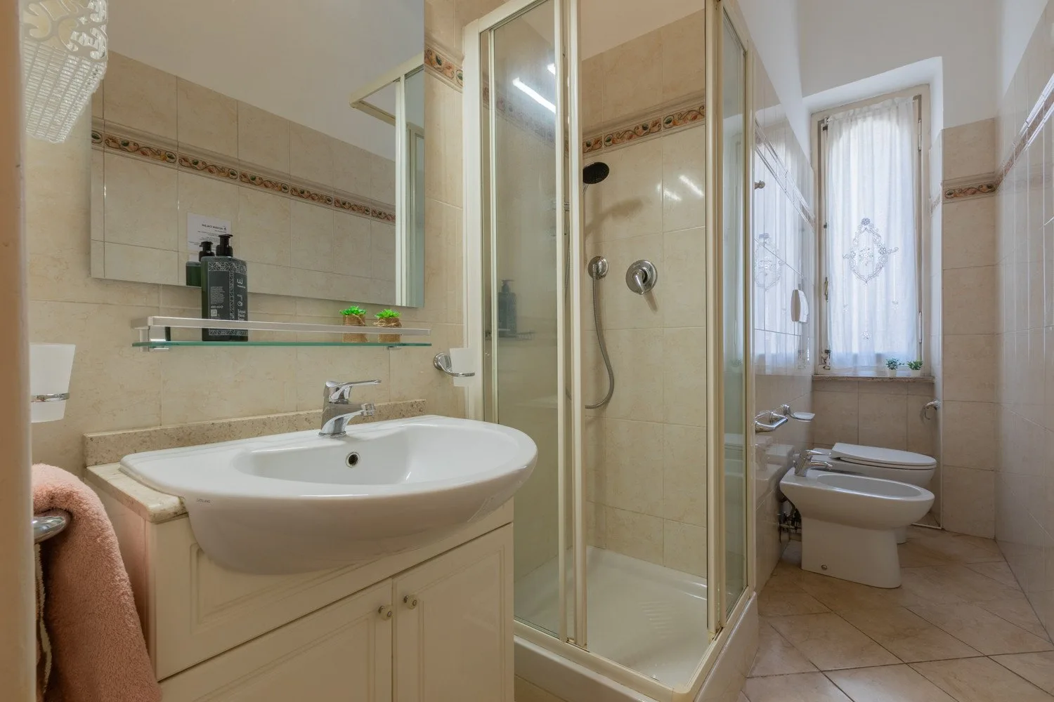 Un baño alicatado con lavabo, ducha de vidrio y ventana.