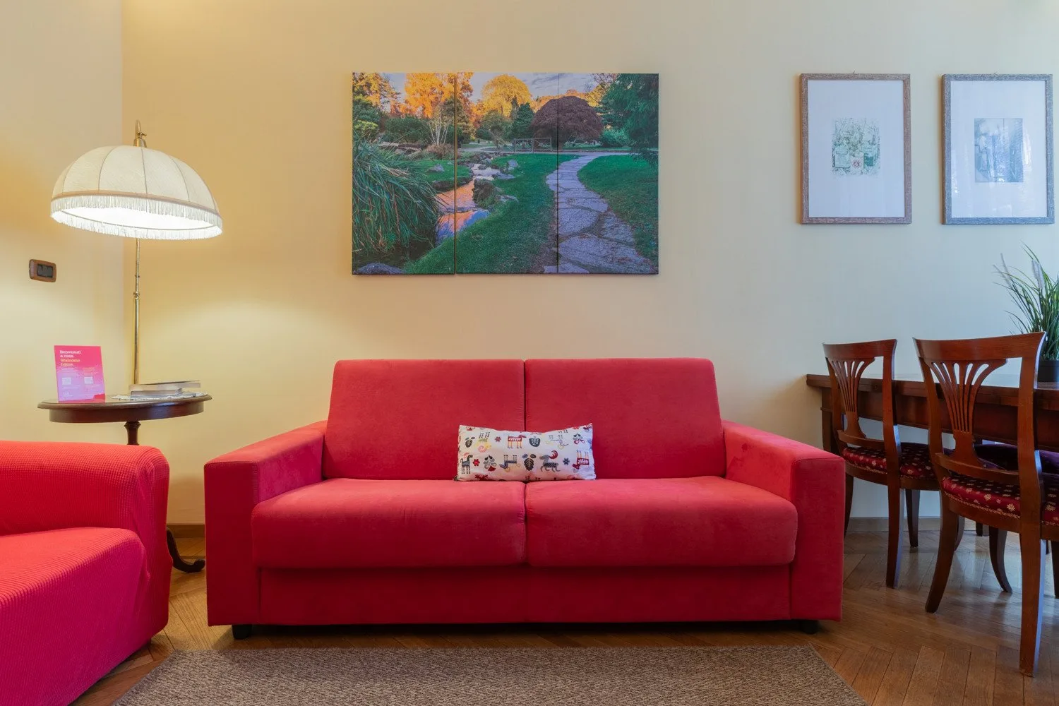 Una sala de estar con asientos rojos, una lámpara de pie y cuadros en la pared.