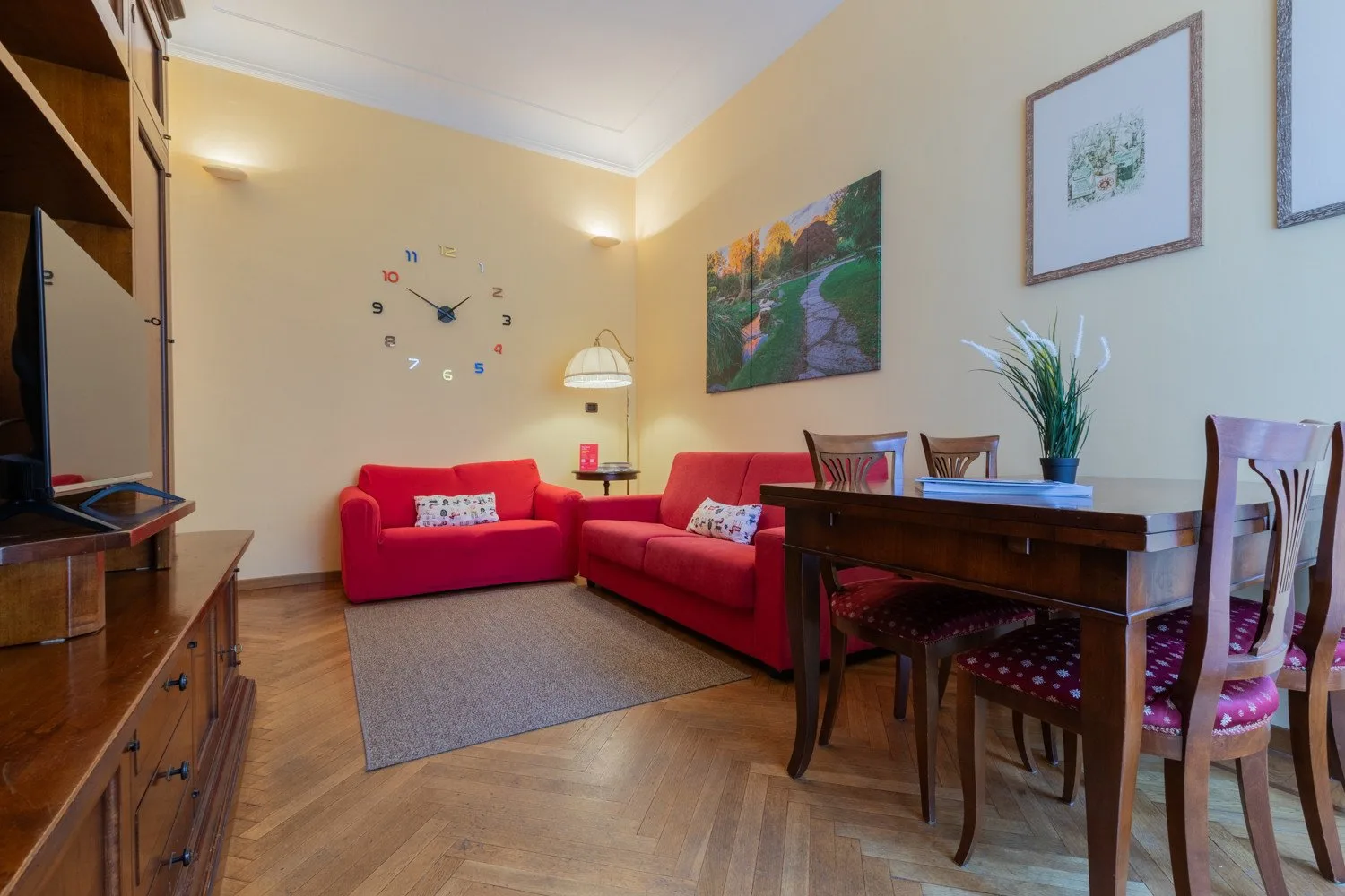 Sala de estar y comedor con sofás rojos, una mesa de madera y cuadros enmarcados.