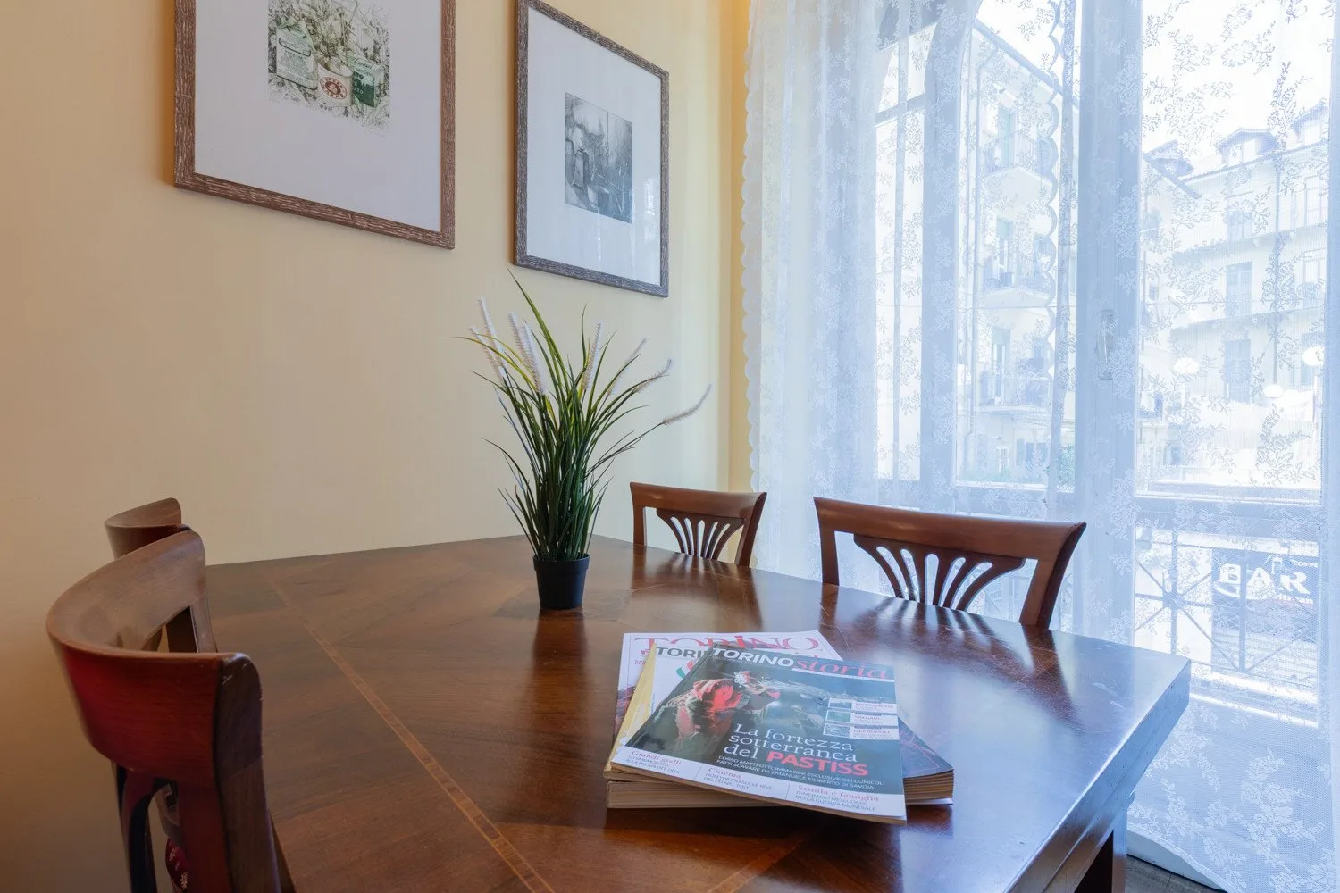 Un comedor con una mesa de madera, asientos y una gran ventana con cortinas.