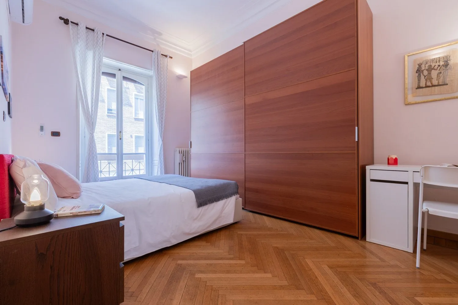 Un dormitorio con una cama junto a un armario grande de madera y una ventana luminosa.