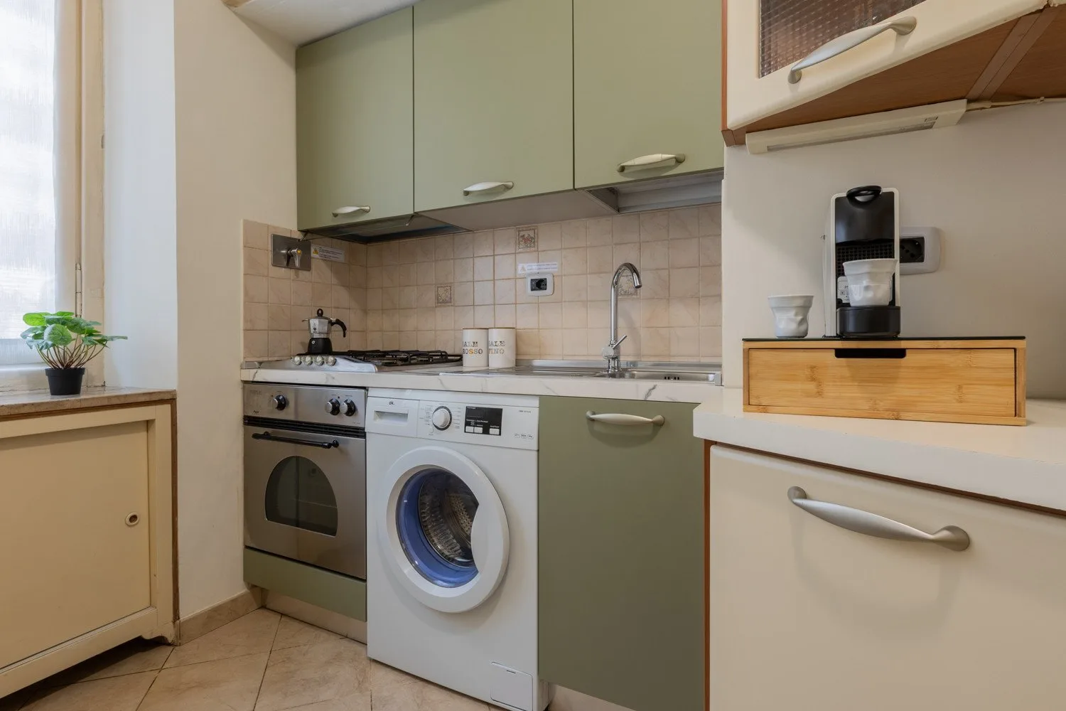 Una cocina compacta con armarios verdes, una estufa y una lavadora.