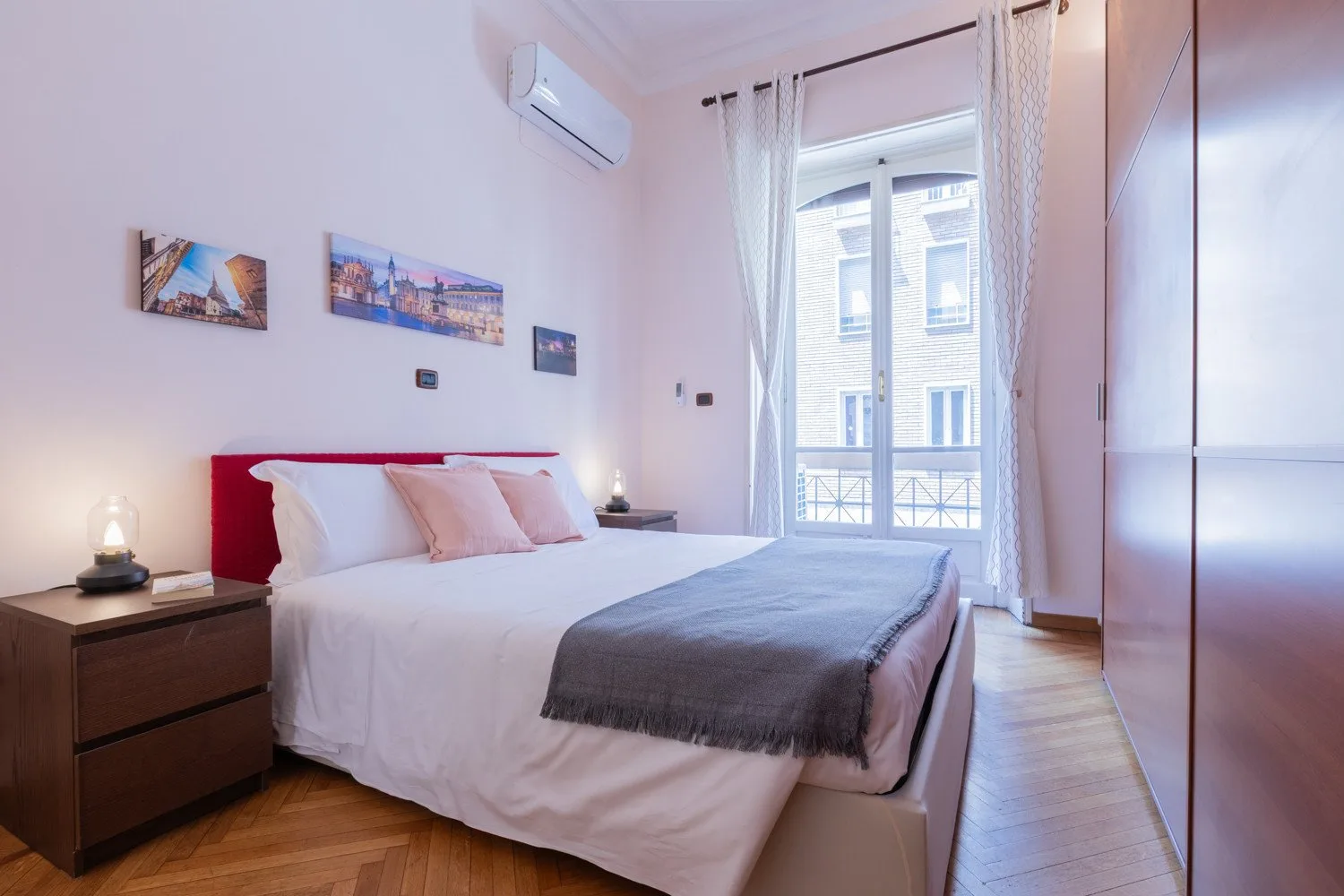 Un dormitorio con una cama, mesitas de noche y una ventana alta con cortinas.