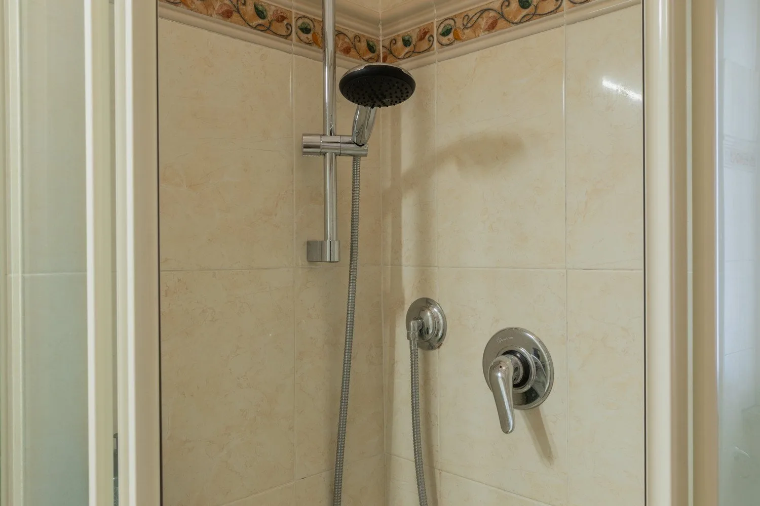 Una ducha con azulejos, ducha de mano y controles montados en la pared.