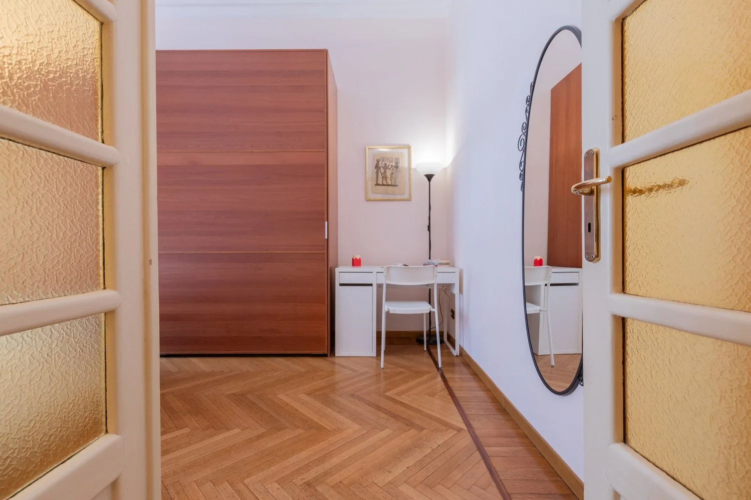 Una habitación luminosa con escritorio, silla, armario y espejo de pared.