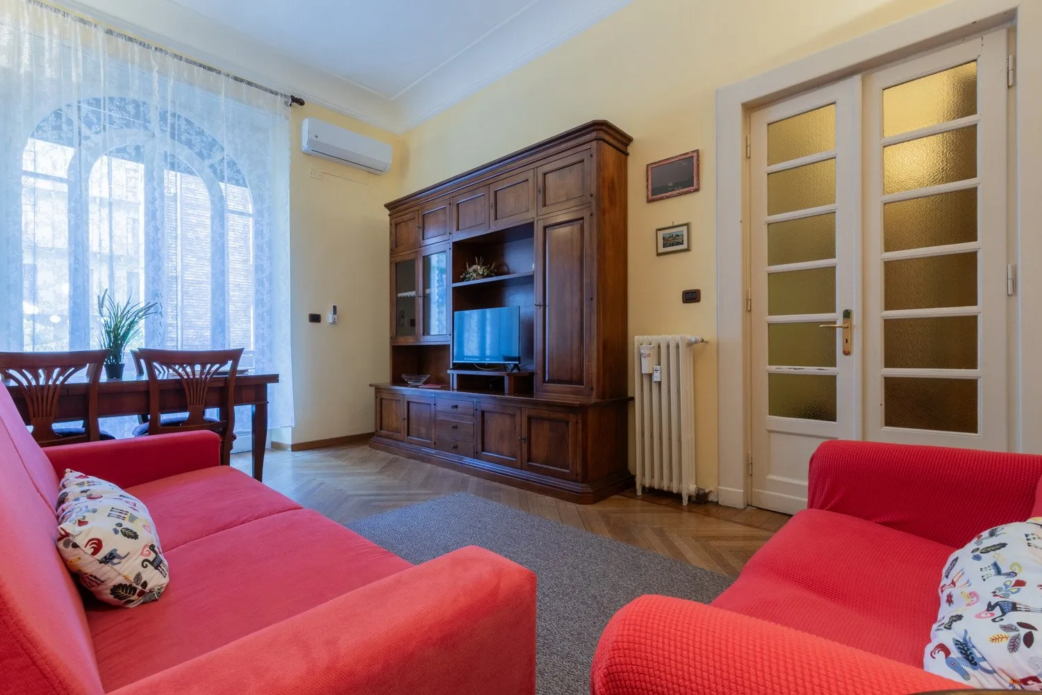 Una sala de estar con asientos rojos, un mueble de madera y un comedor junto a la ventana.