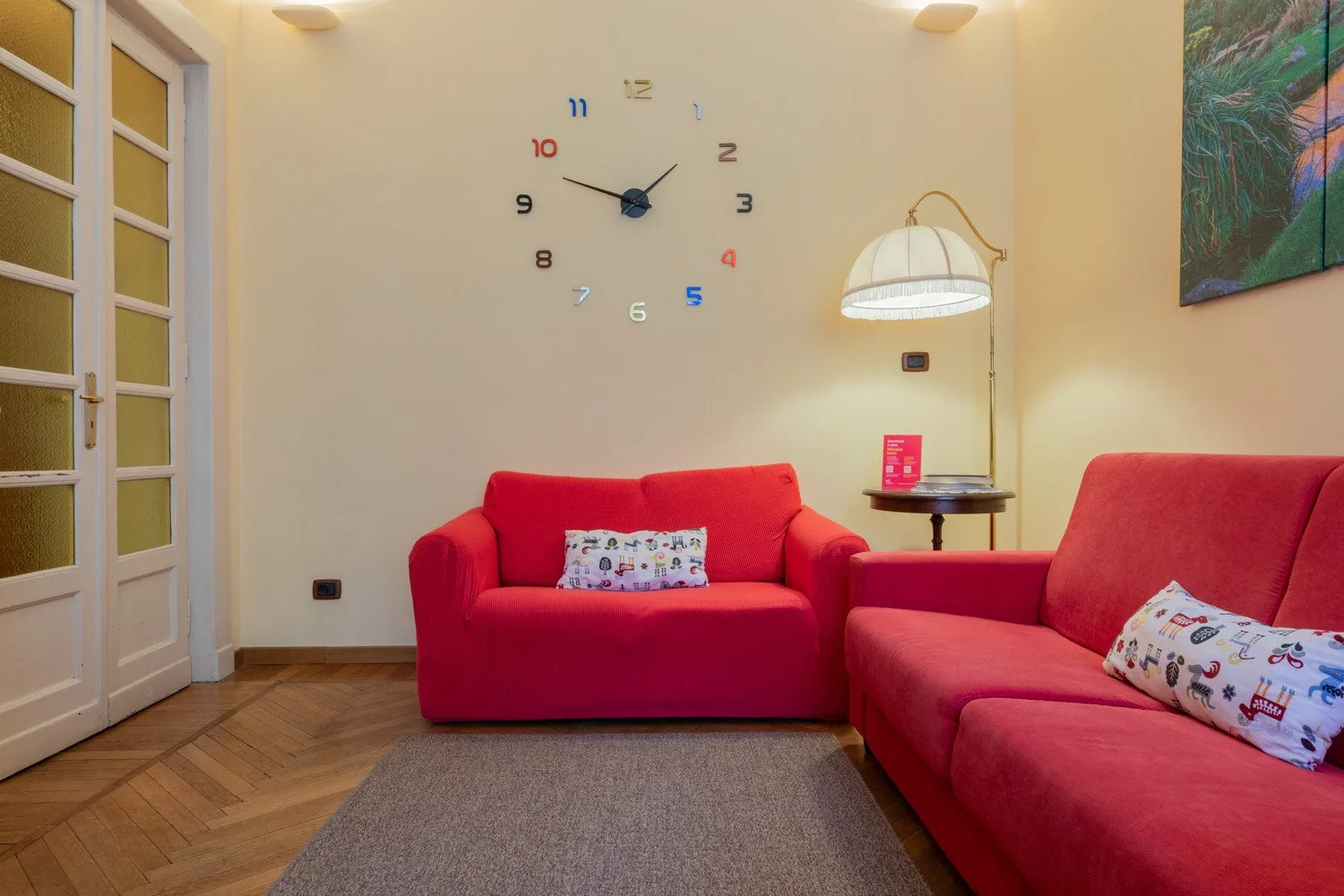 Una sala de estar con asientos rojos, una lámpara de pie y un reloj de pared.