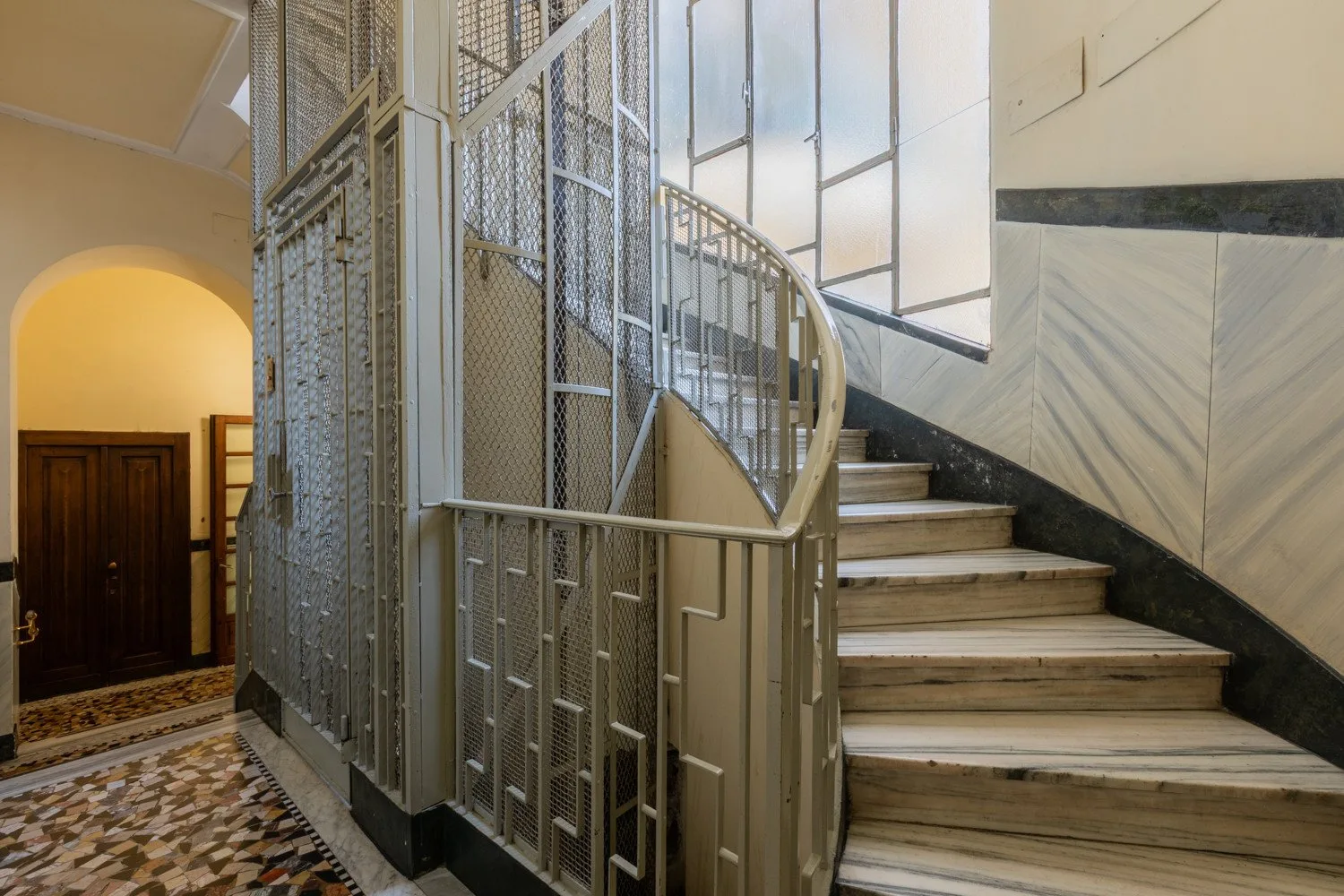 Una escalera interior curva junto a un cerramiento metálico de ascensor.