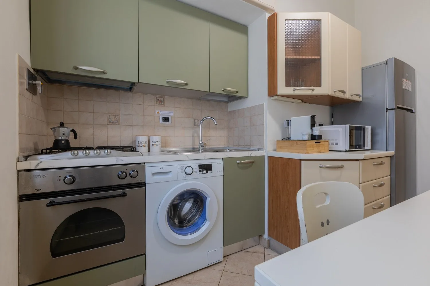 Una cocina compacta con armarios verdes, una cocina y una lavadora.