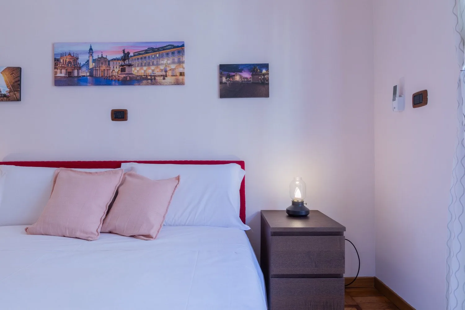 Un dormitorio con una cama tendida y cuadros enmarcados en la pared.