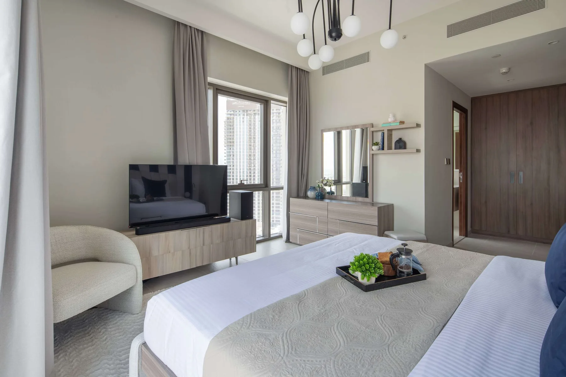 Un dormitorio luminoso con una cama grande, televisor y tocador junto a la ventana.