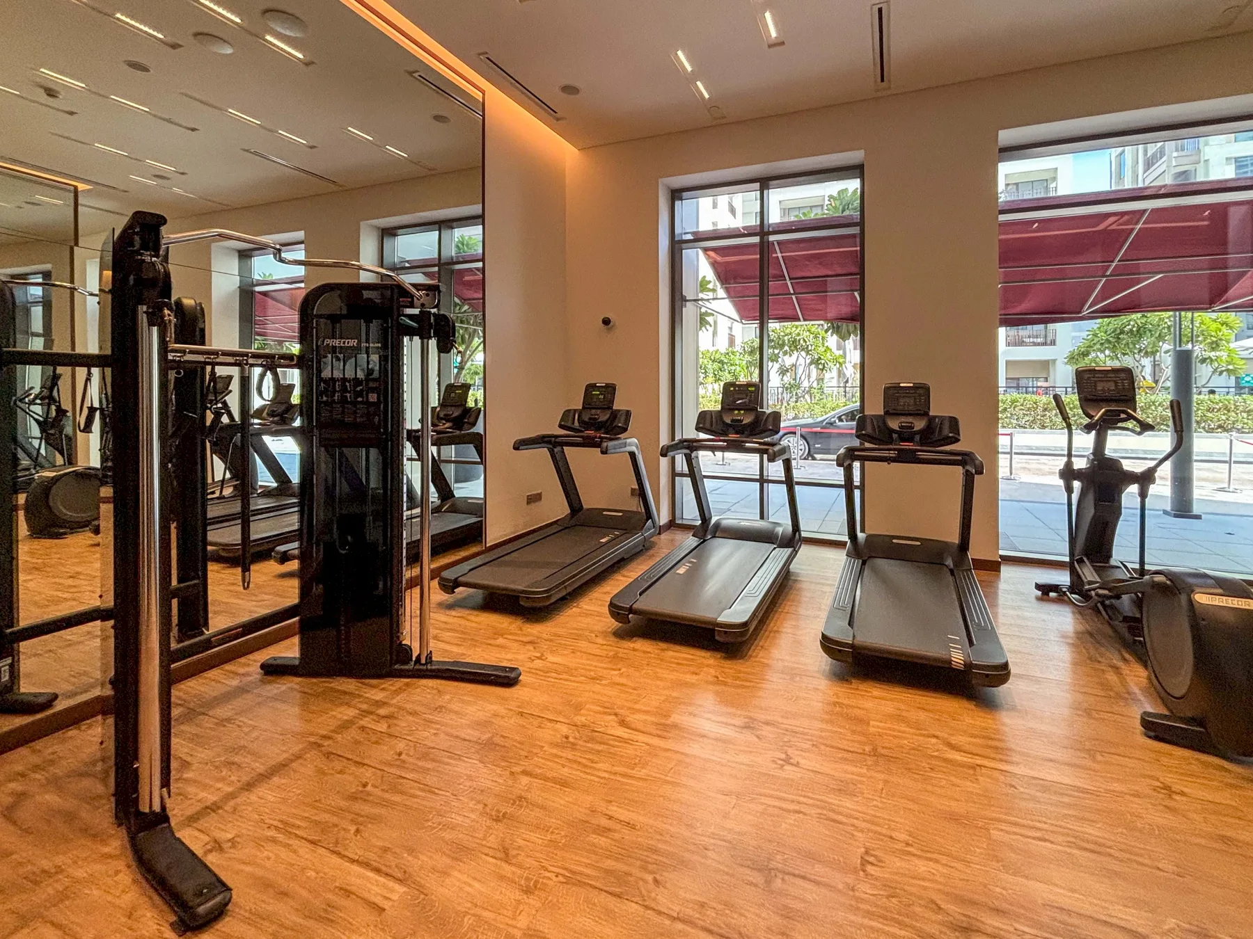 Un gimnasio con máquinas de ejercicio y cintas de correr junto a grandes ventanas.