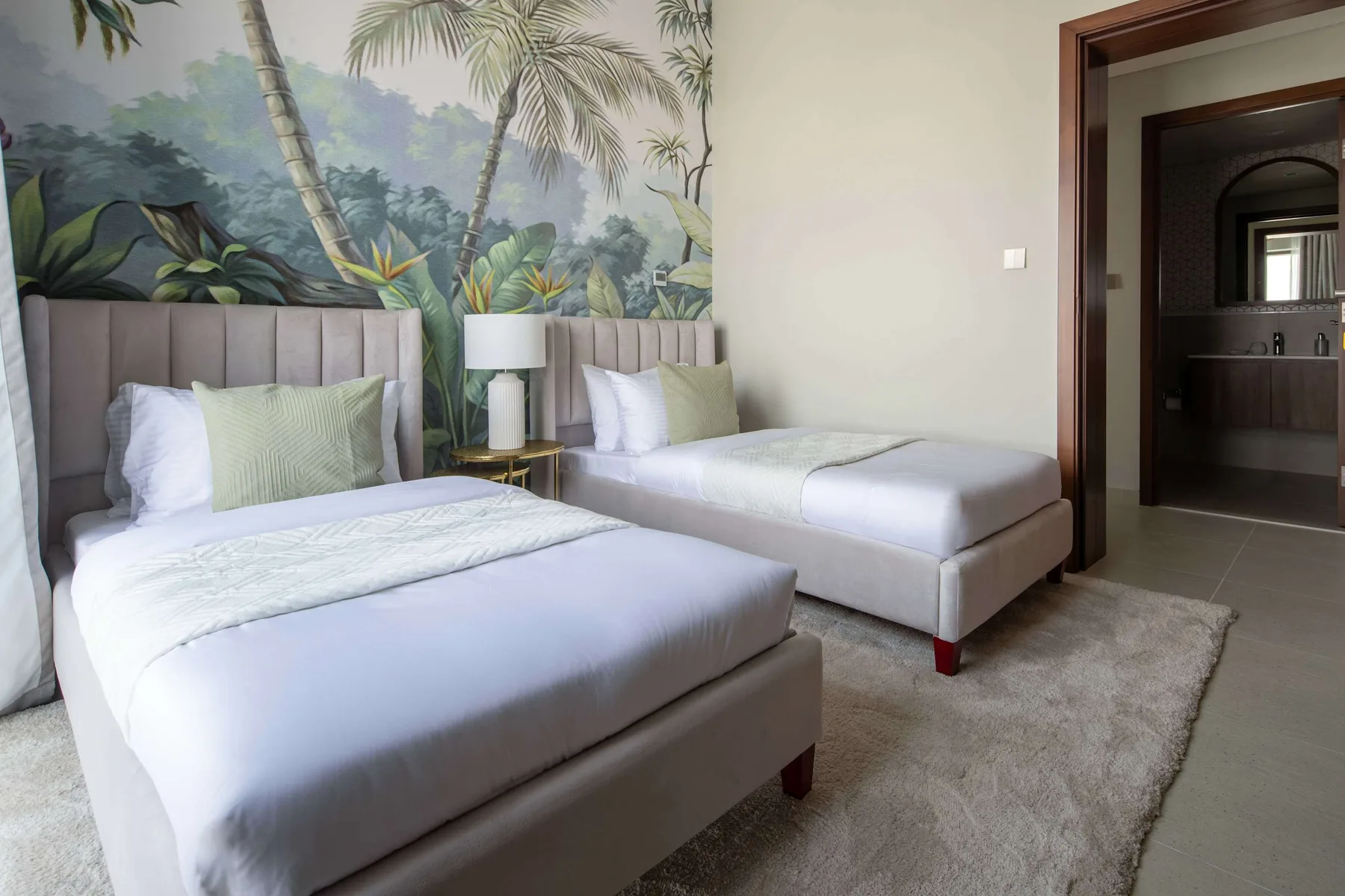 Un dormitorio con dos camas, ropa de cama clara y un mural tropical.