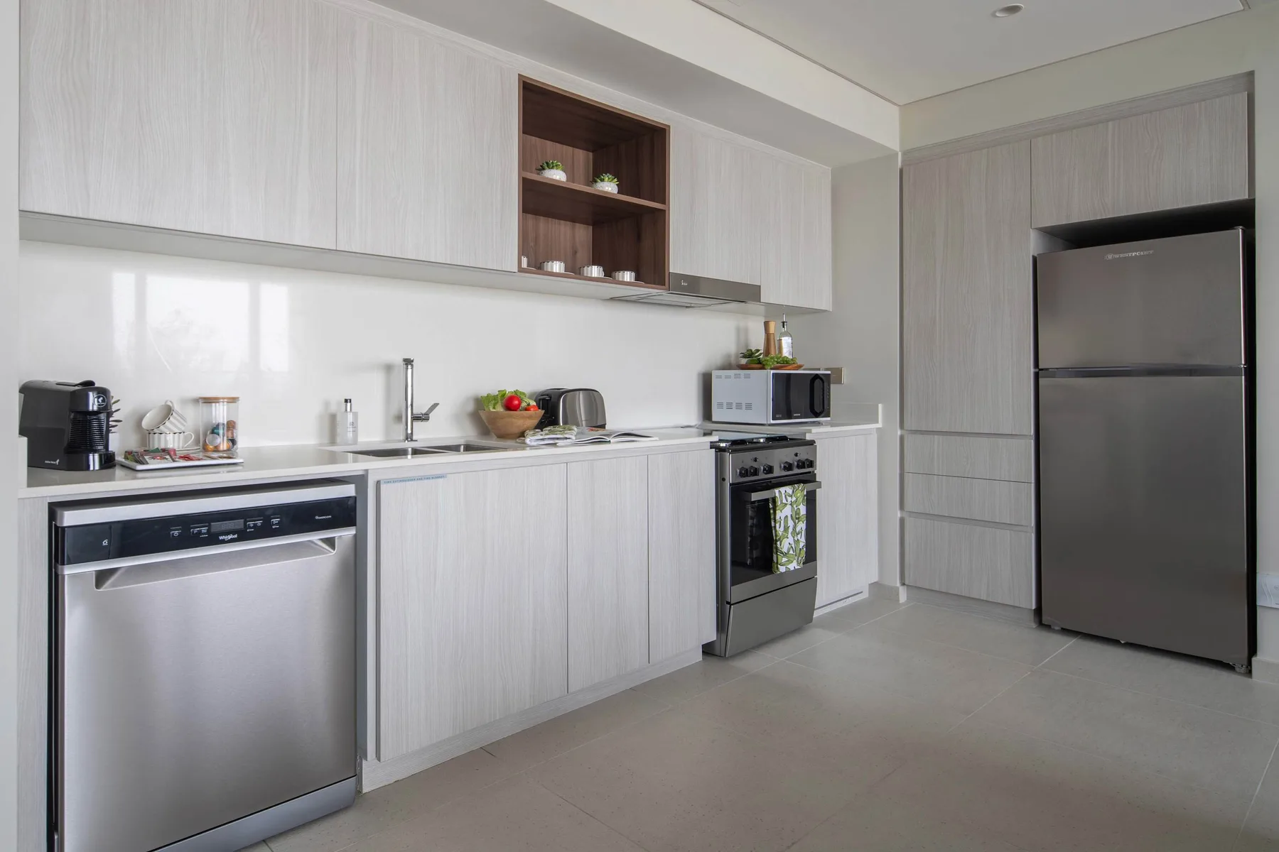Una cocina moderna con gabinetes claros, un refrigerador y electrodomésticos de acero inoxidable.