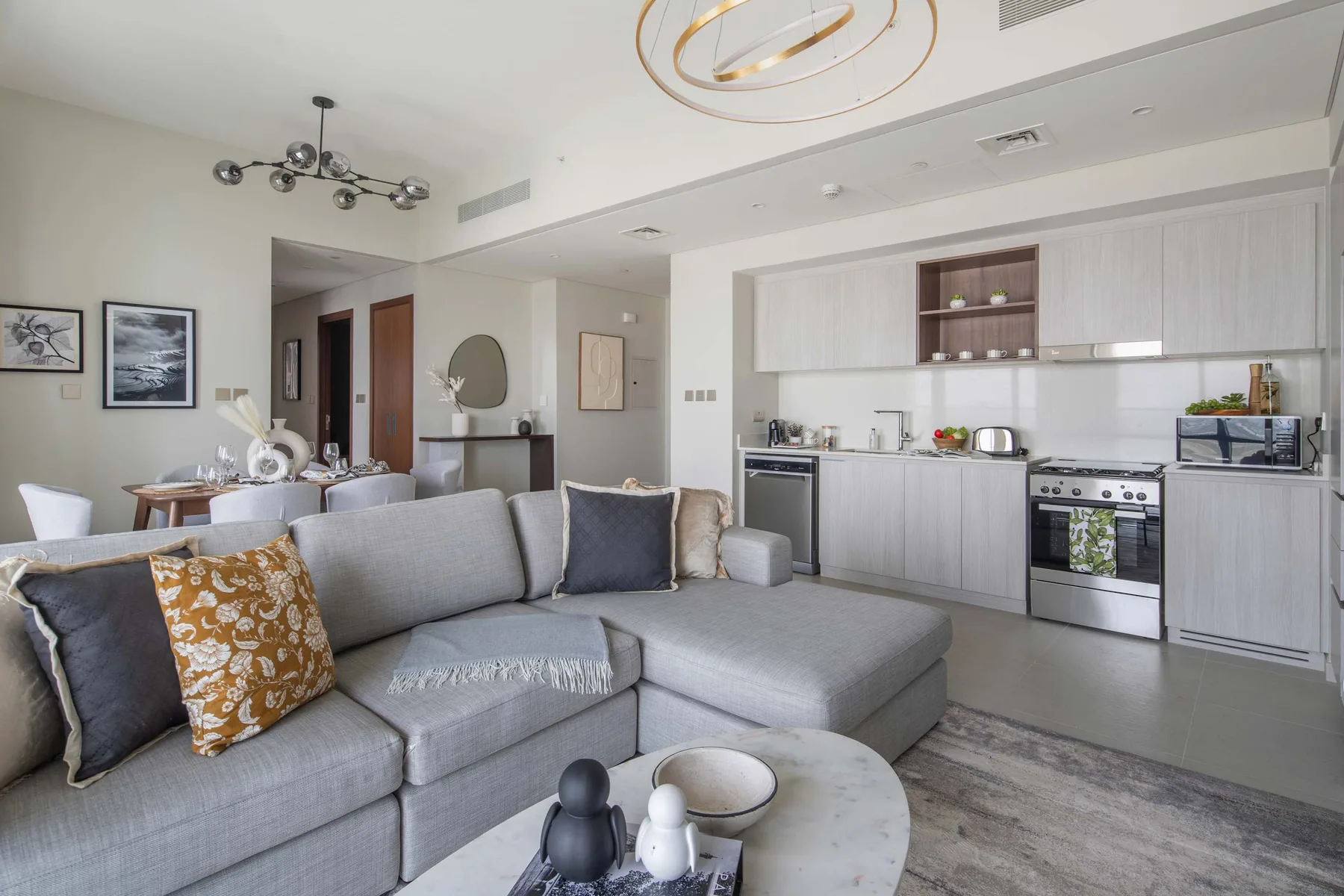 An open-plan living room and kitchen with gray seating and light cabinets.