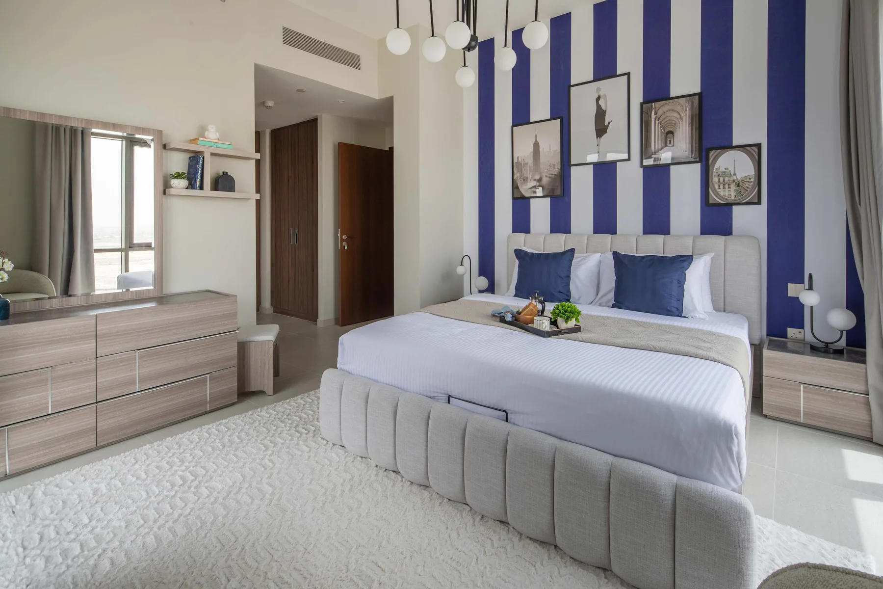 Un dormitorio con una cama grande, una pared de franjas azules y blancas y mesitas de noche a juego.