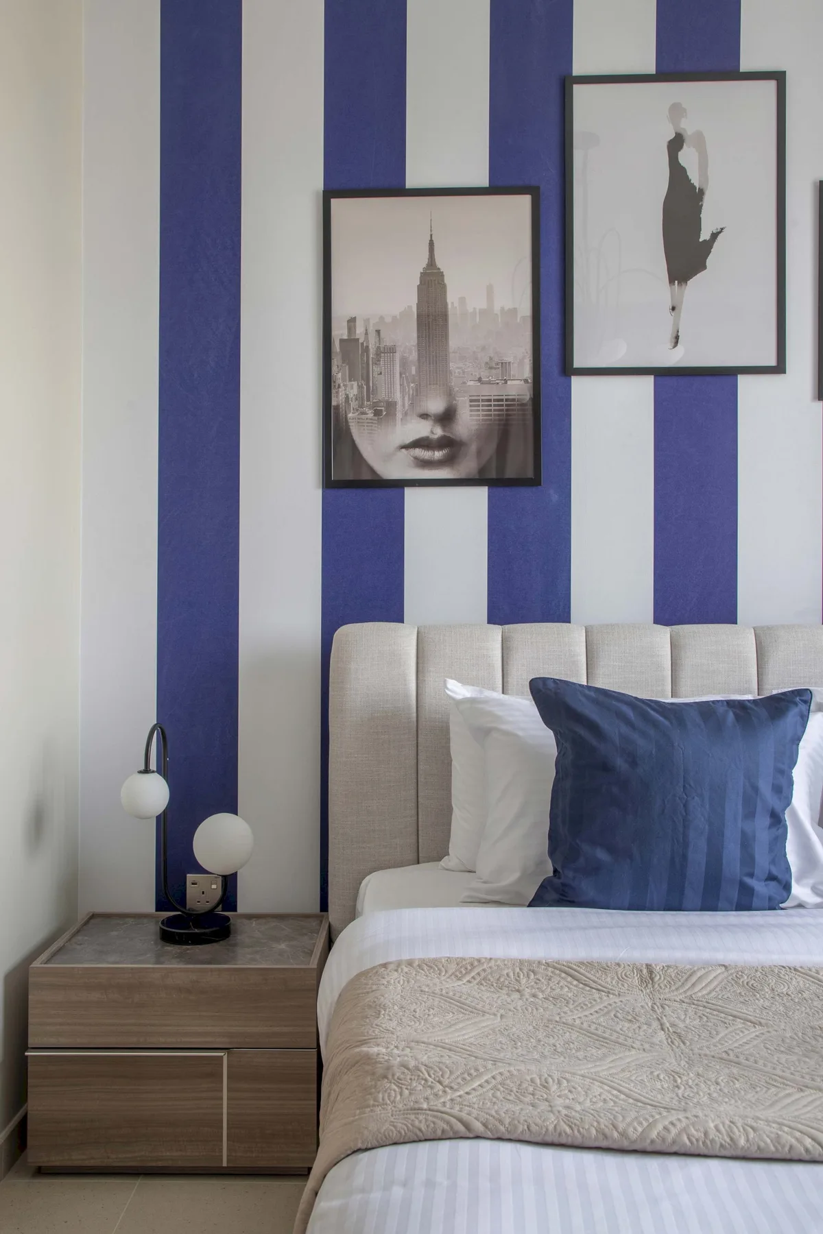 Un dormitorio con una cama arreglada junto a una pared de rayas azules y blancas.