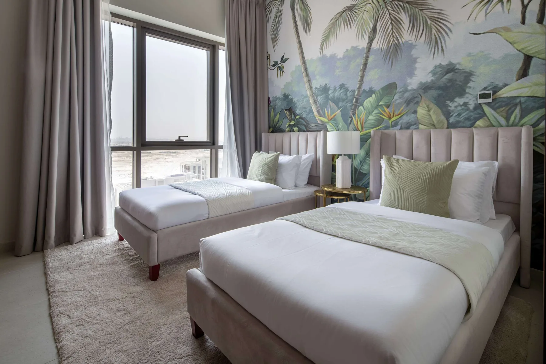 Un dormitorio con dos camas, mesitas de noche y un mural tropical.