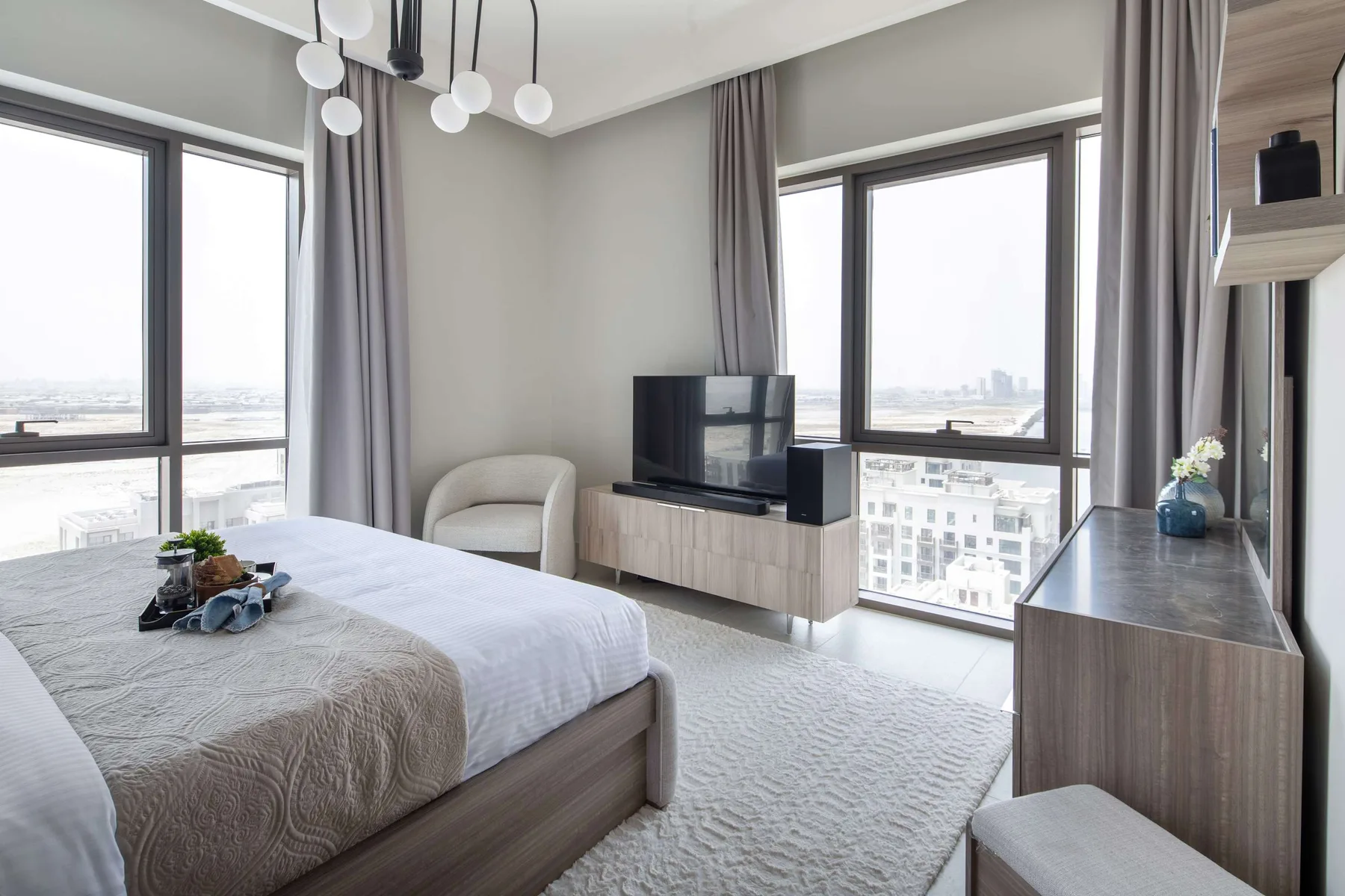 Un dormitorio luminoso con cama, televisor y grandes ventanas con vistas a la ciudad.