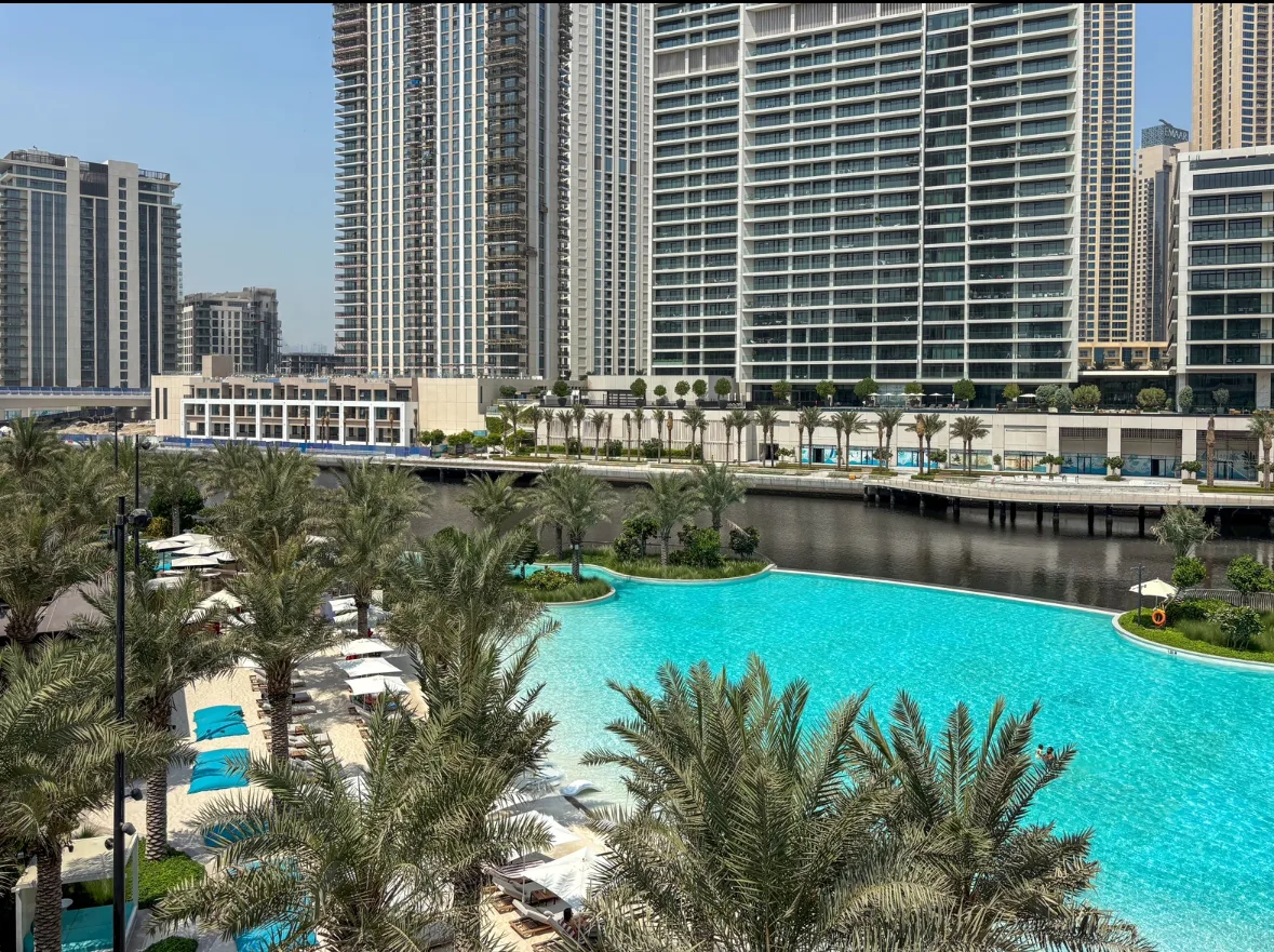 Una piscina turquesa está rodeada de palmeras y altos edificios residenciales.