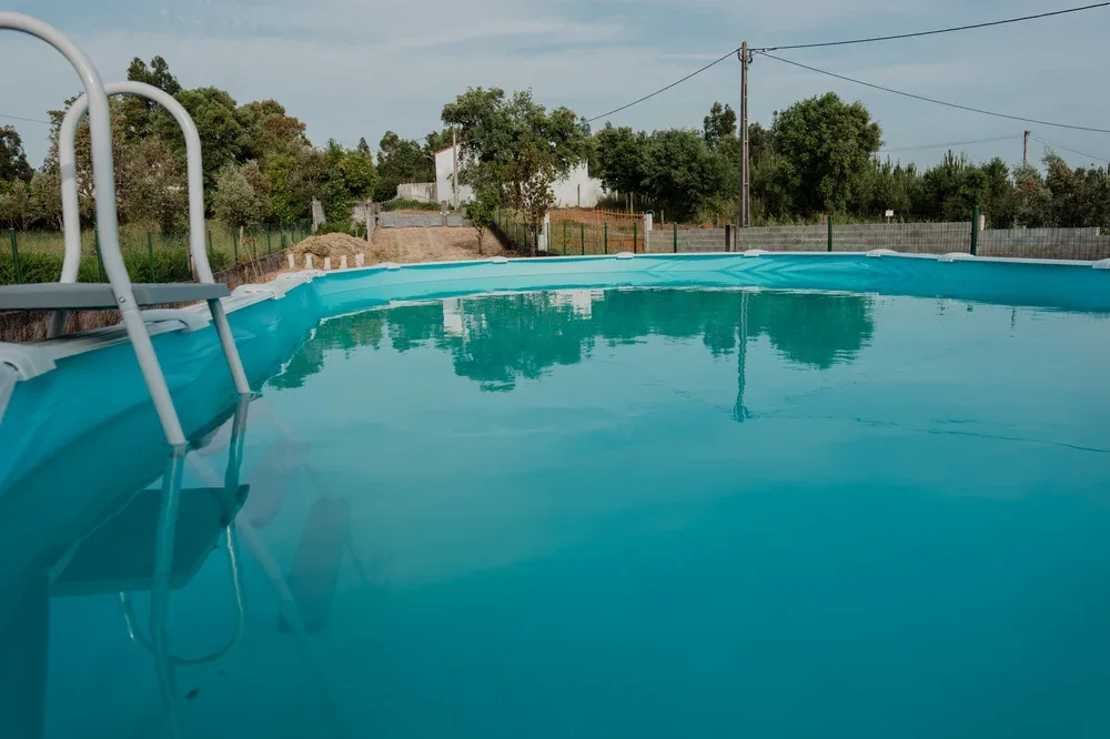 Una piscina al aire libre refleja los árboles cercanos y la cerca que la rodea.