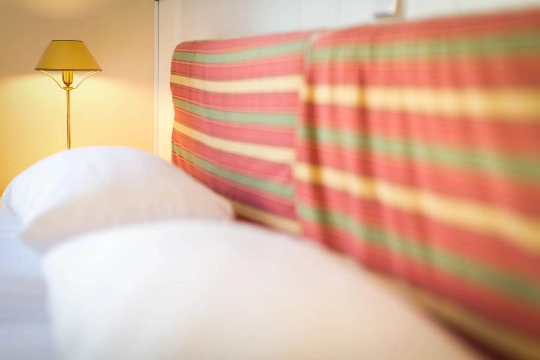 Un dormitorio con ropa de cama blanca junto a un cabecero tapizado a rayas.